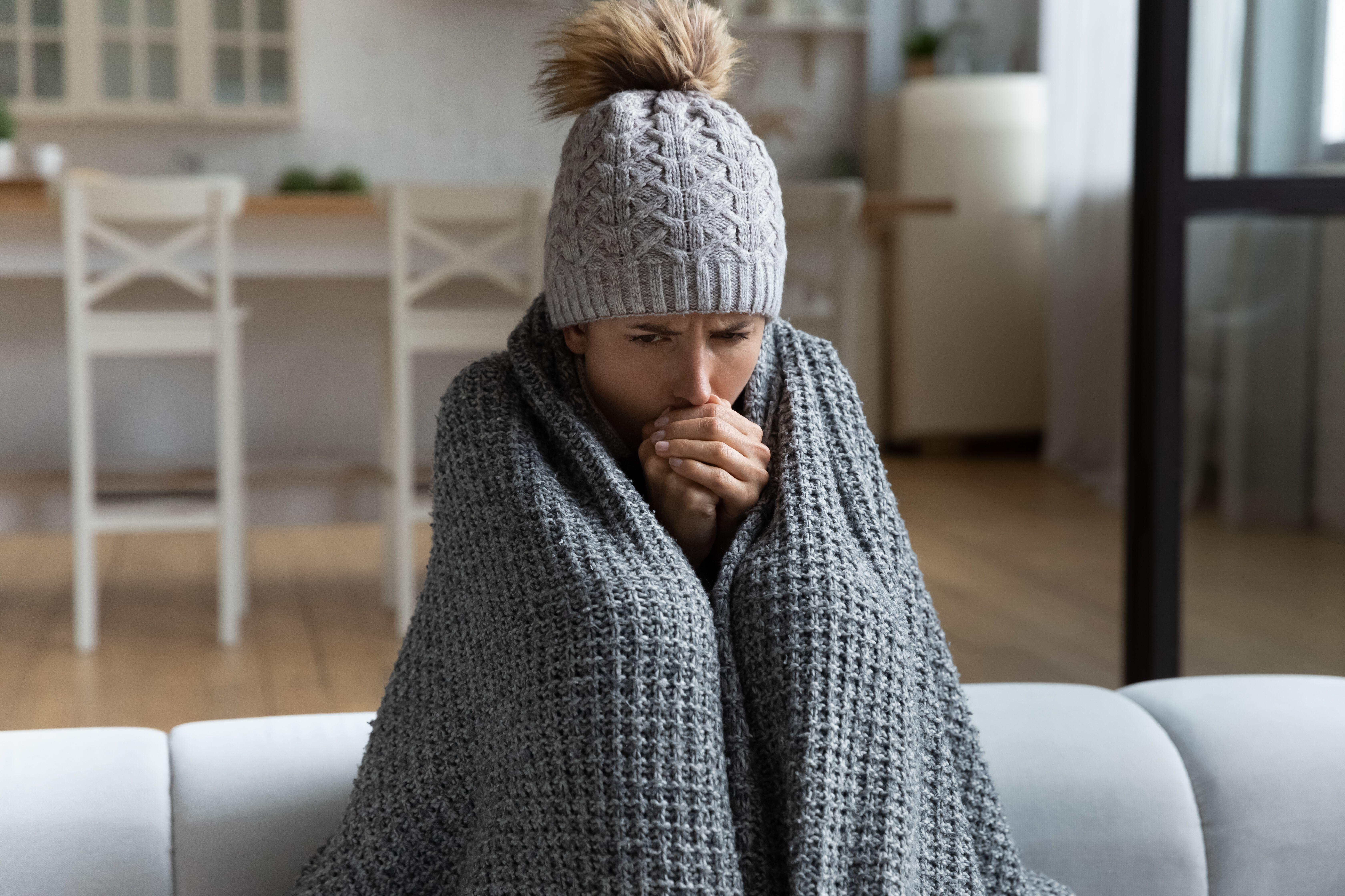 Woman feeling cold at home wearing a woolly hat and blanket