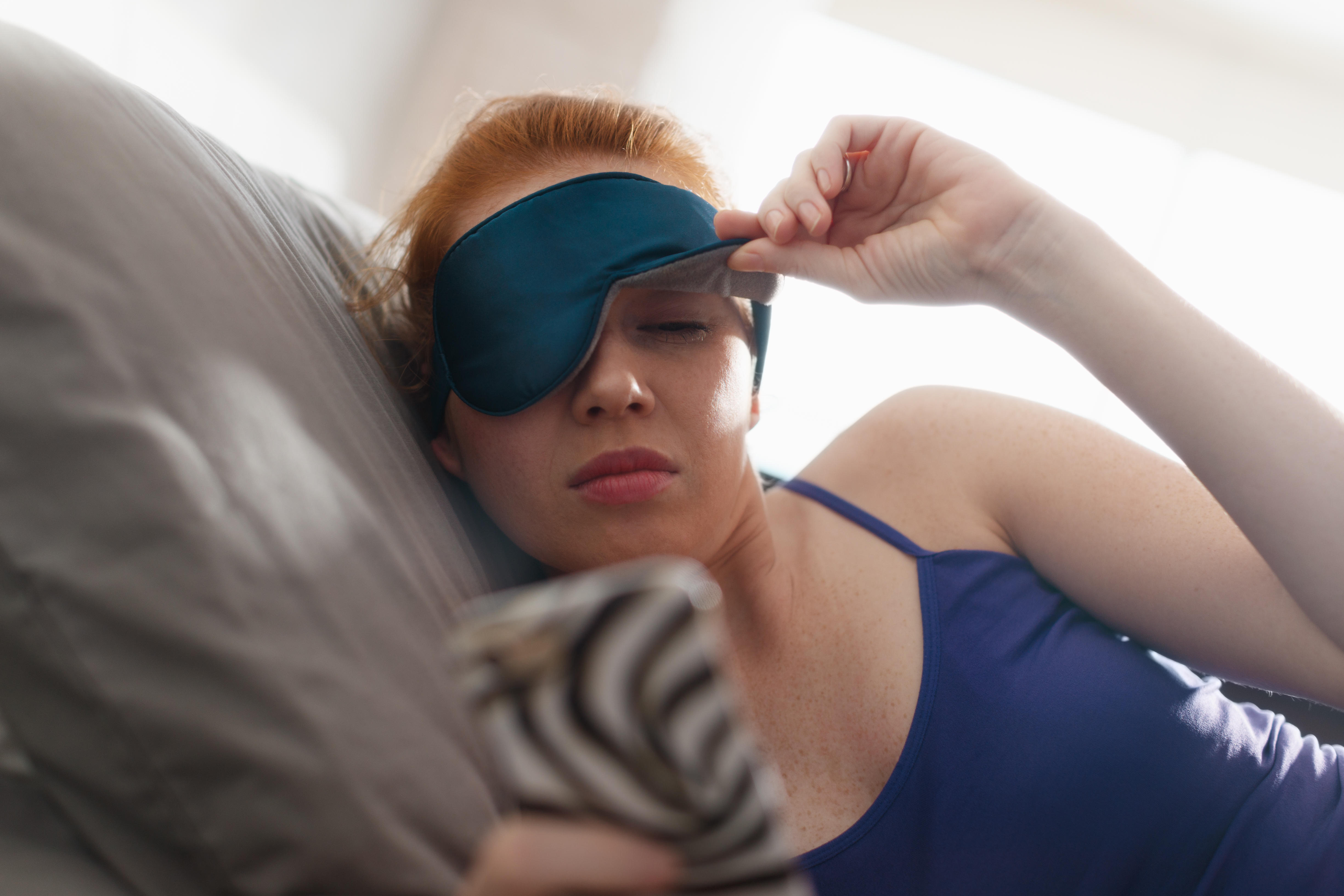 Young woman waking up in bed beginning to take her sleeping mask off