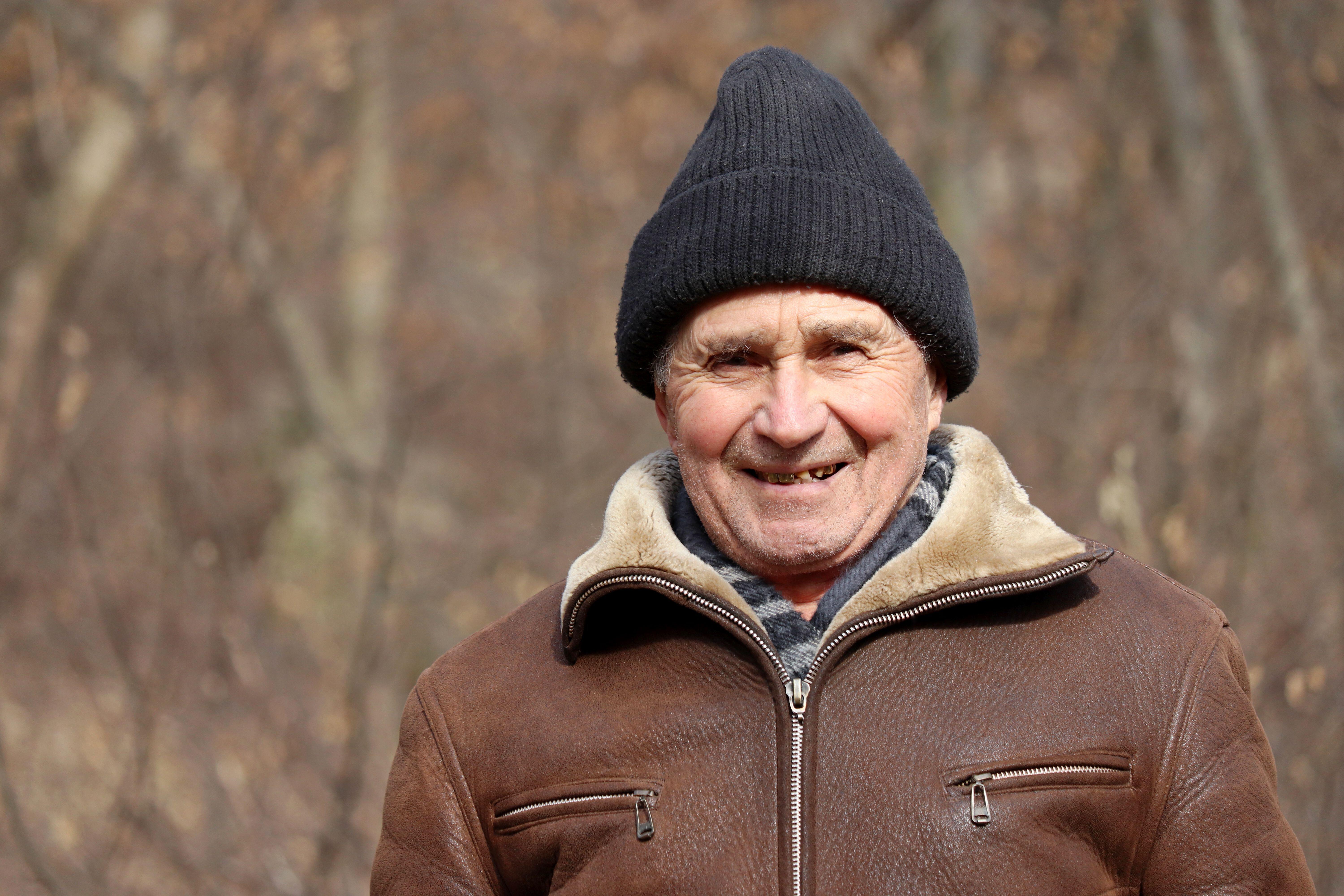 Elderly man wearing hat and coat outdoors smiling 