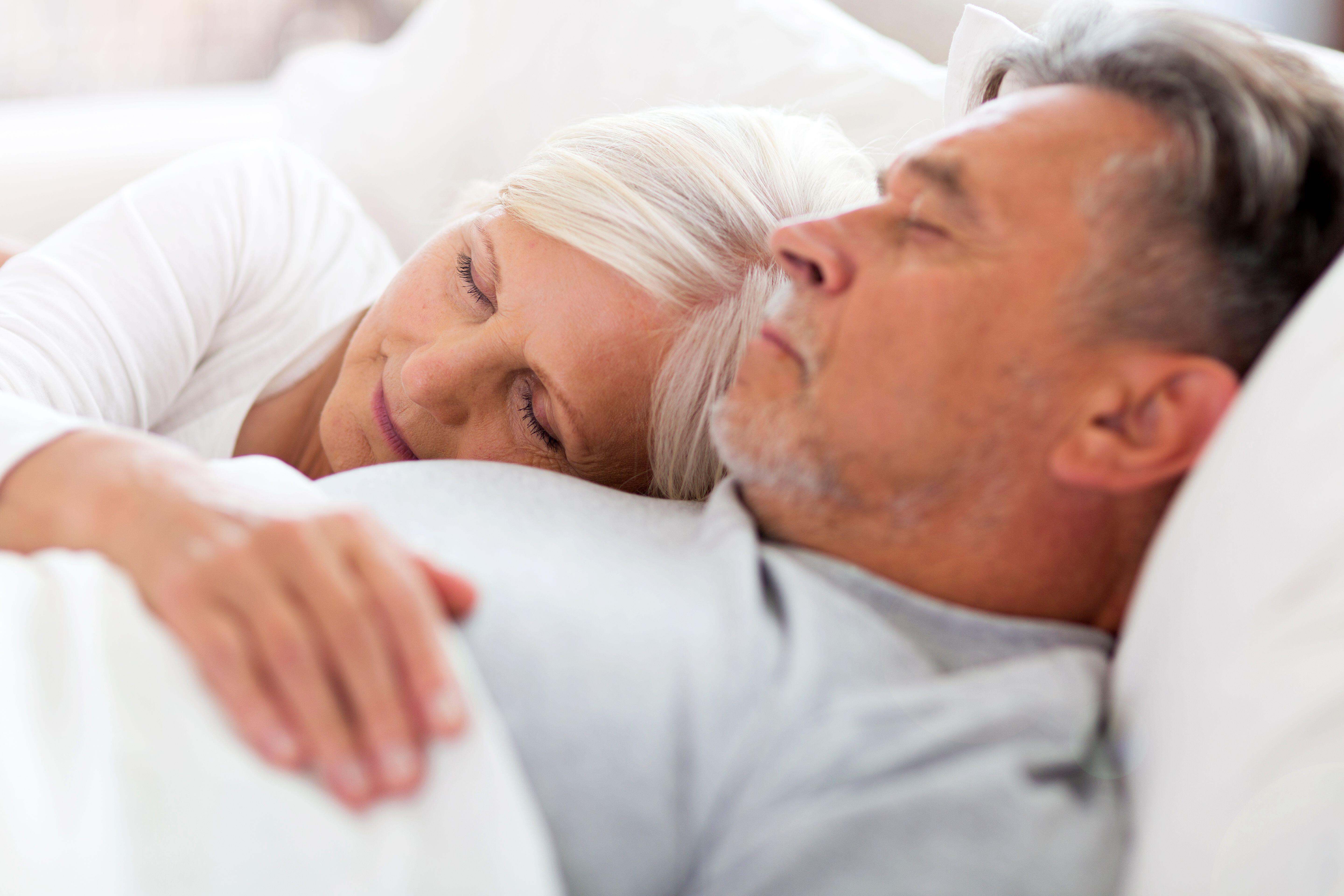 Senior man and woman cuddling in bed together struggling to sleep