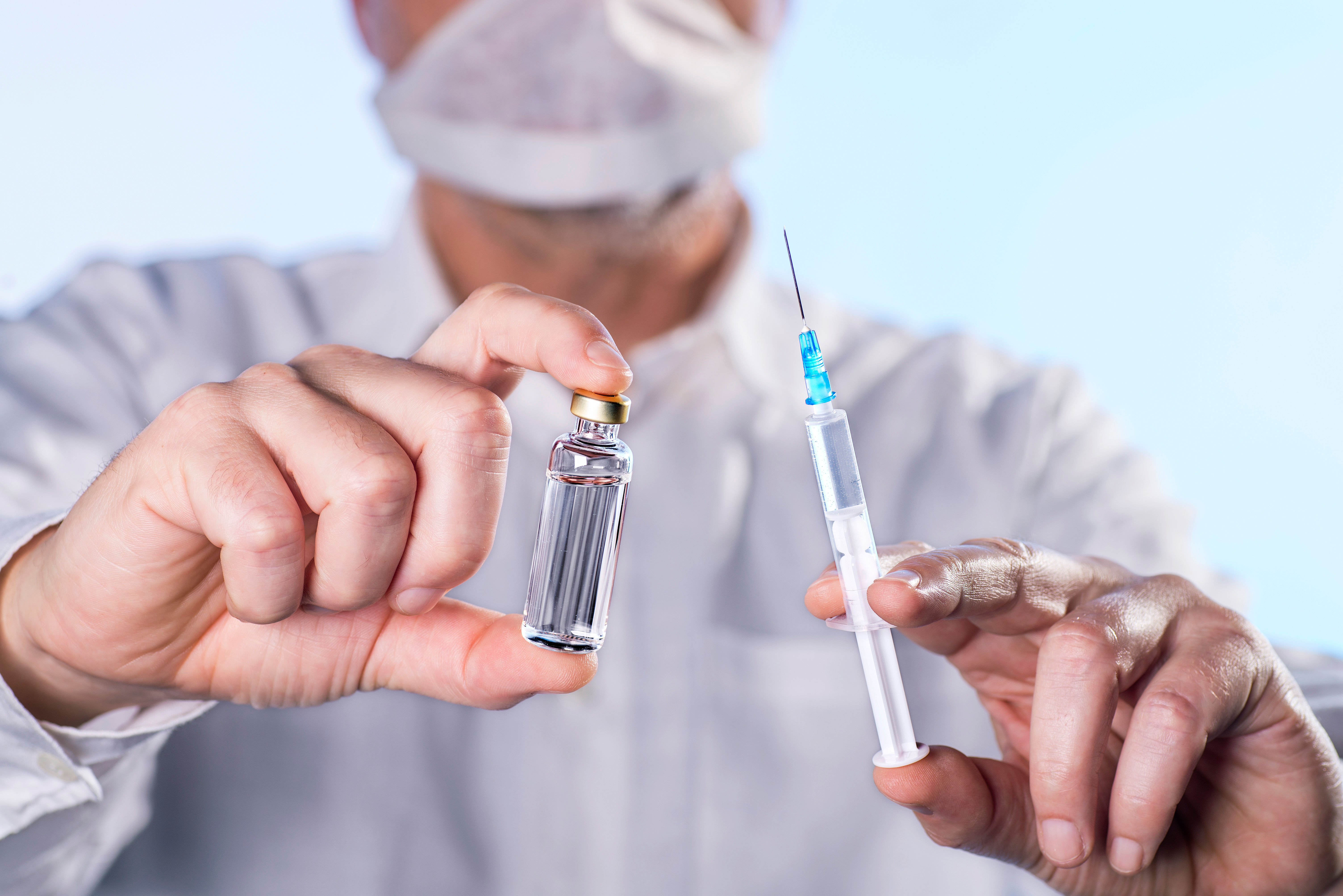 Doctor holding a syringe and a vial of vaccine in their hands.