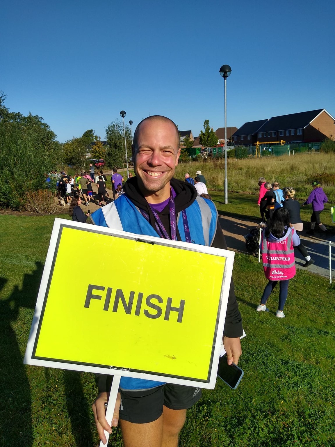 Darren Wood smiling as he holds a finish sign for the Edenbrook parkrun