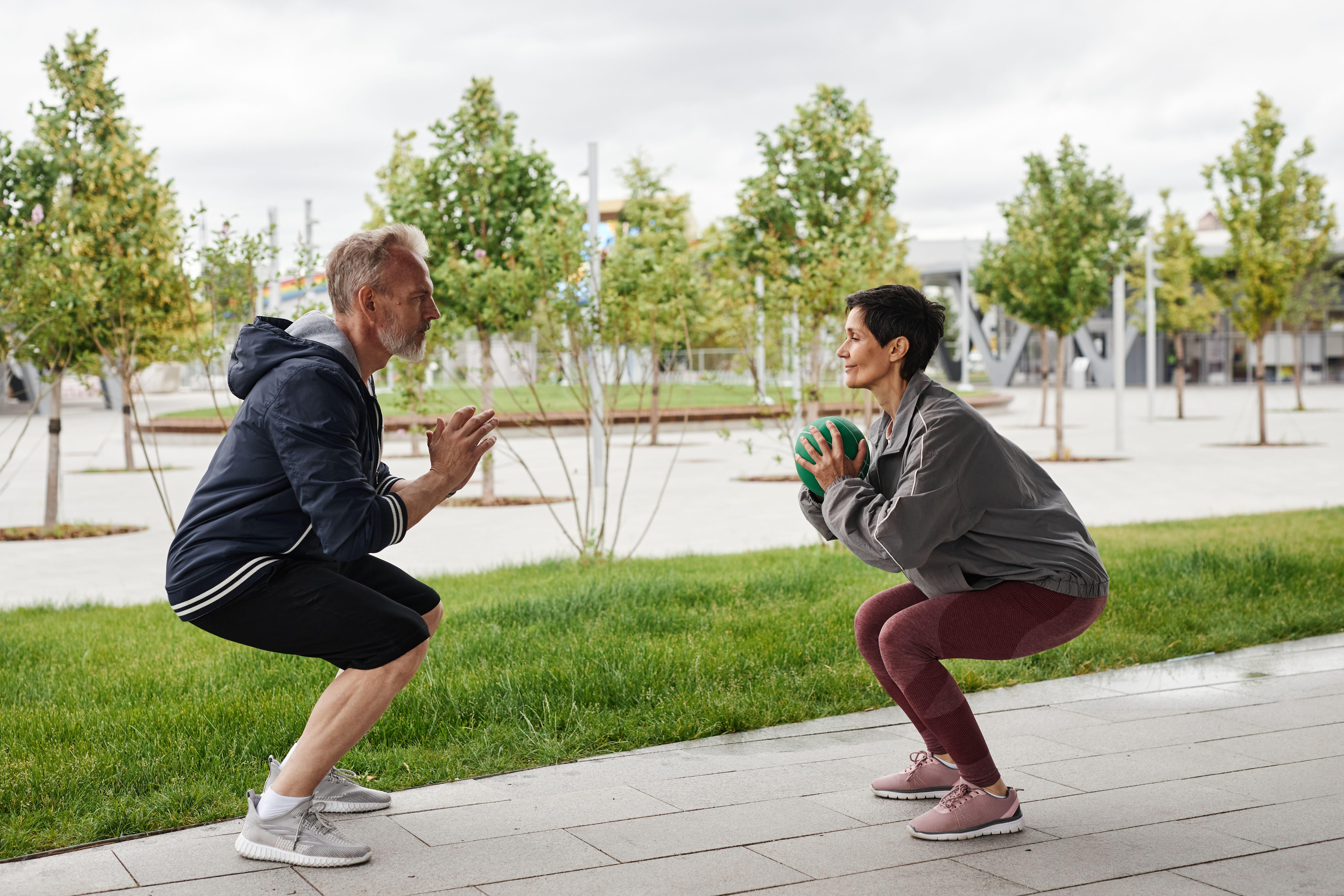 Side view of woman and man in sportswear doing squat jumps passing ball