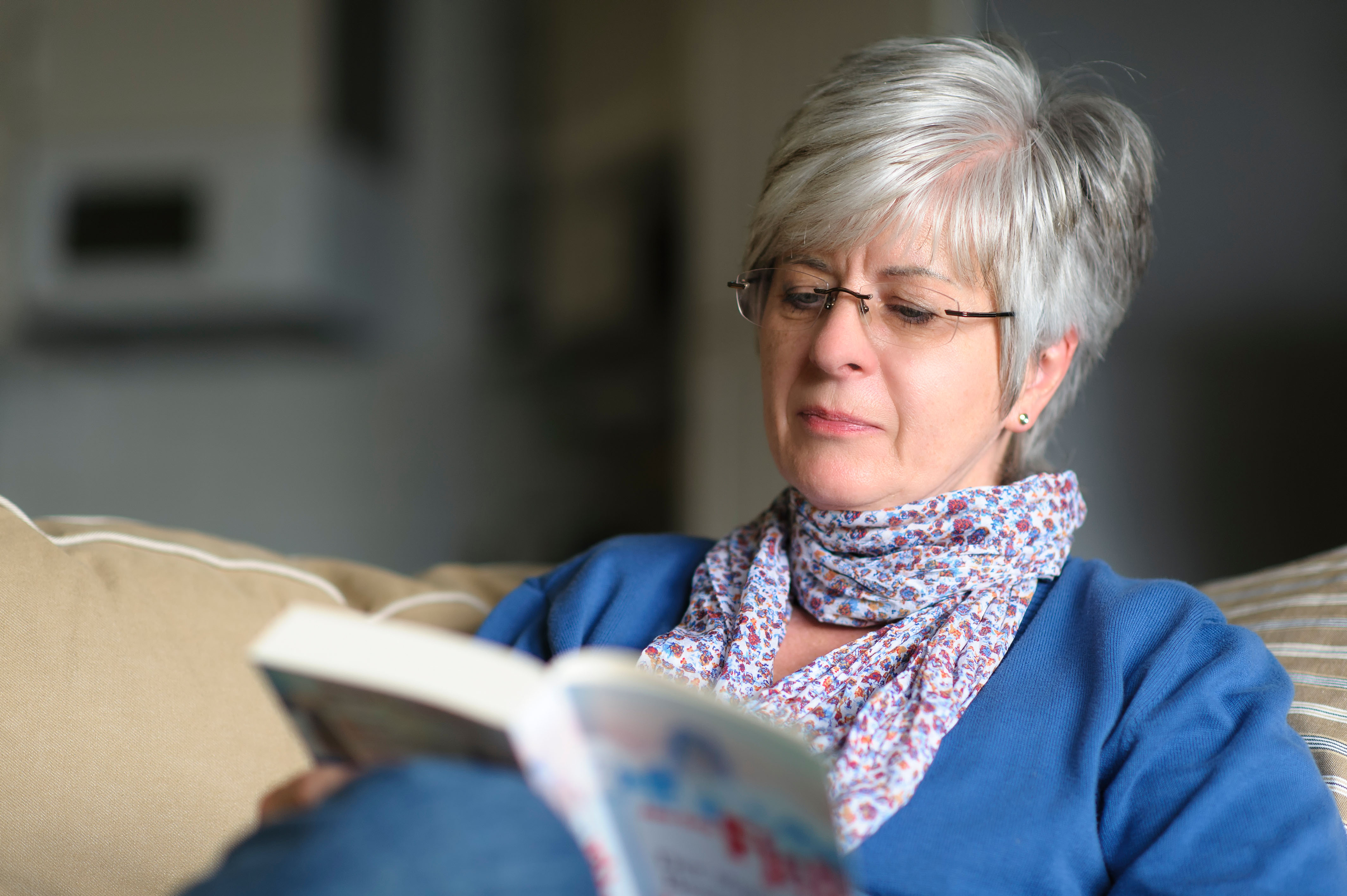 Middle age woman sitting on a sofa reading a book 