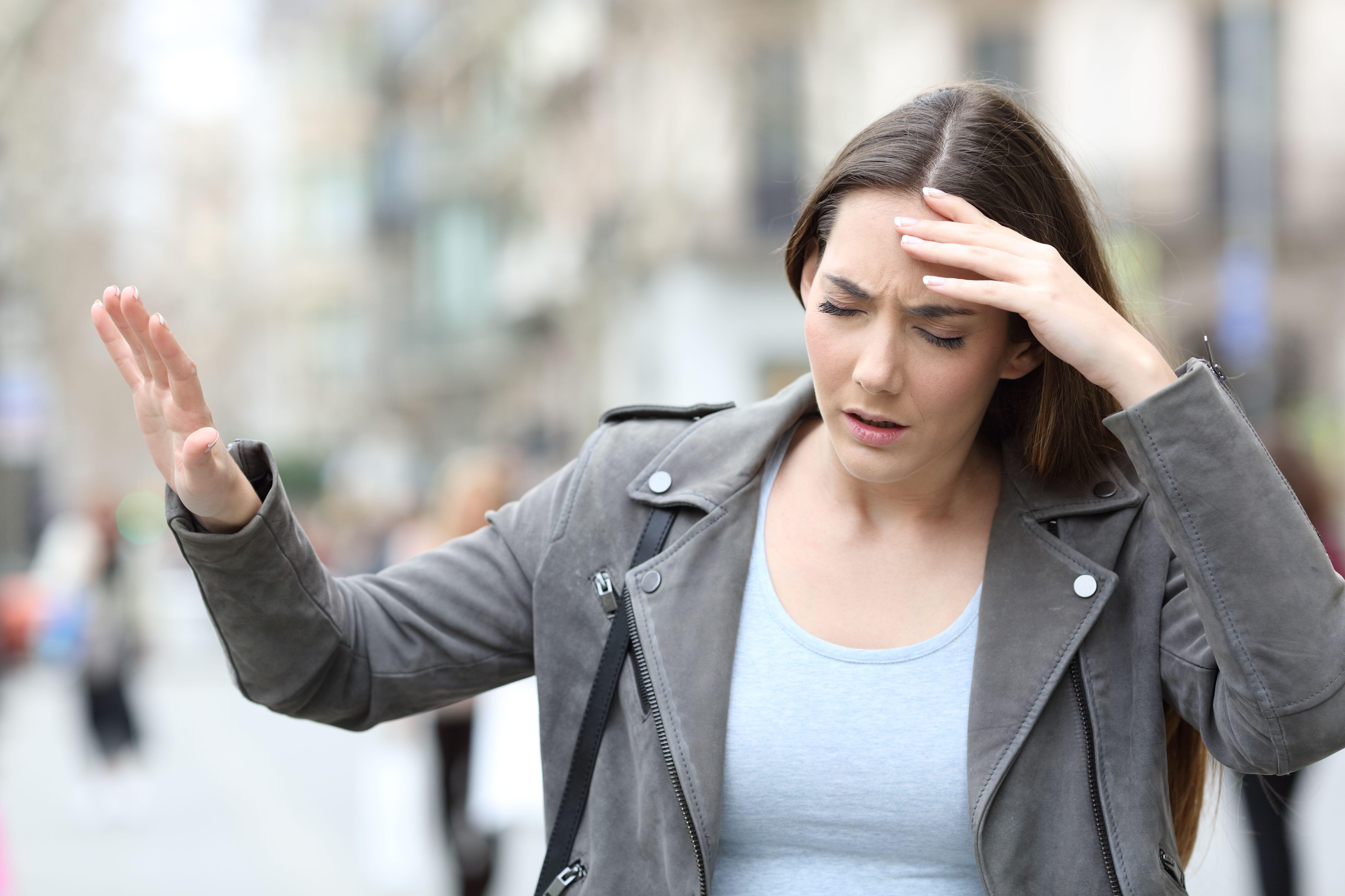 Young woman feeling dizzy and sick on a busy street 