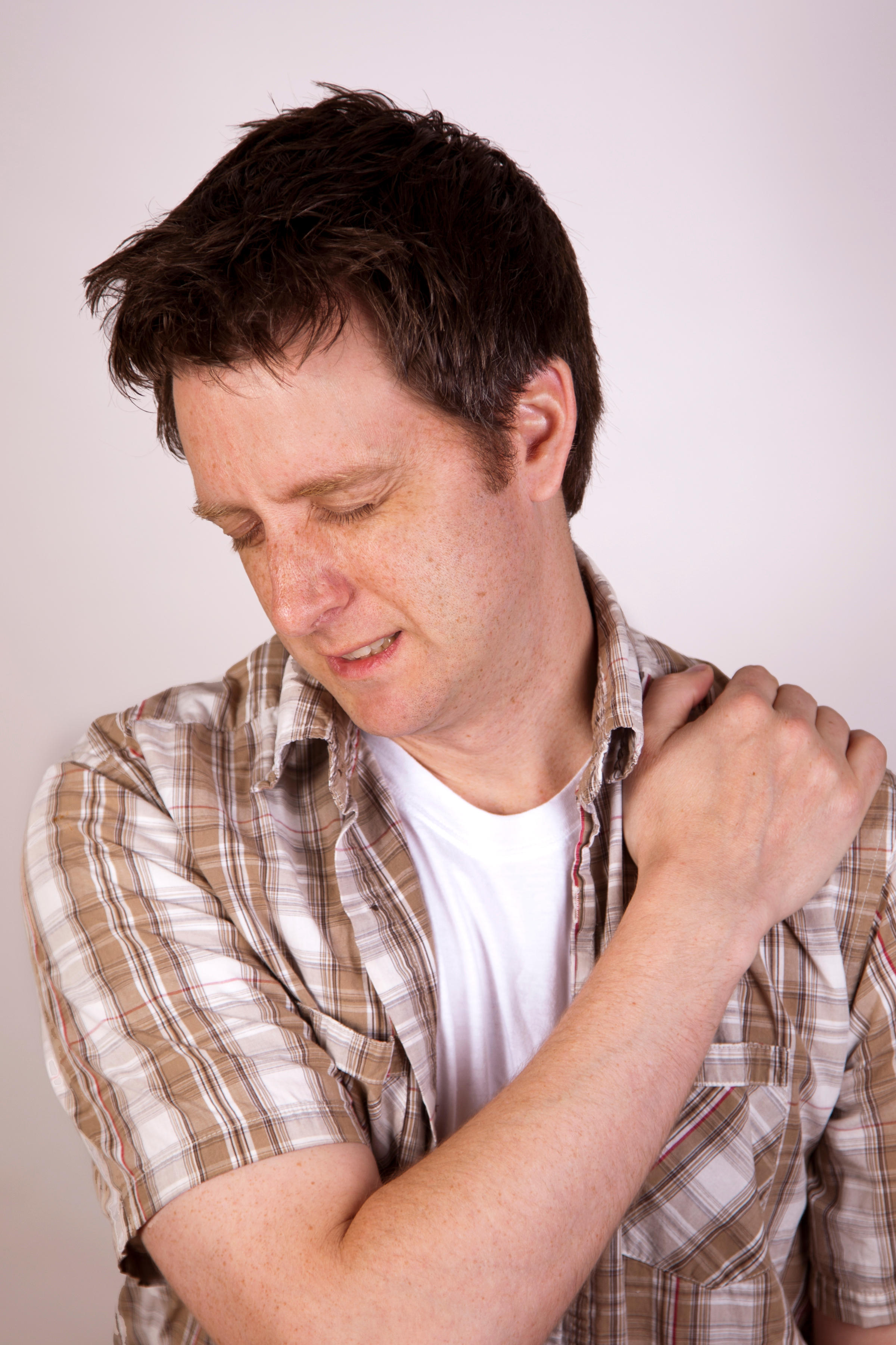 A man grimacing from pain holding his shoulder