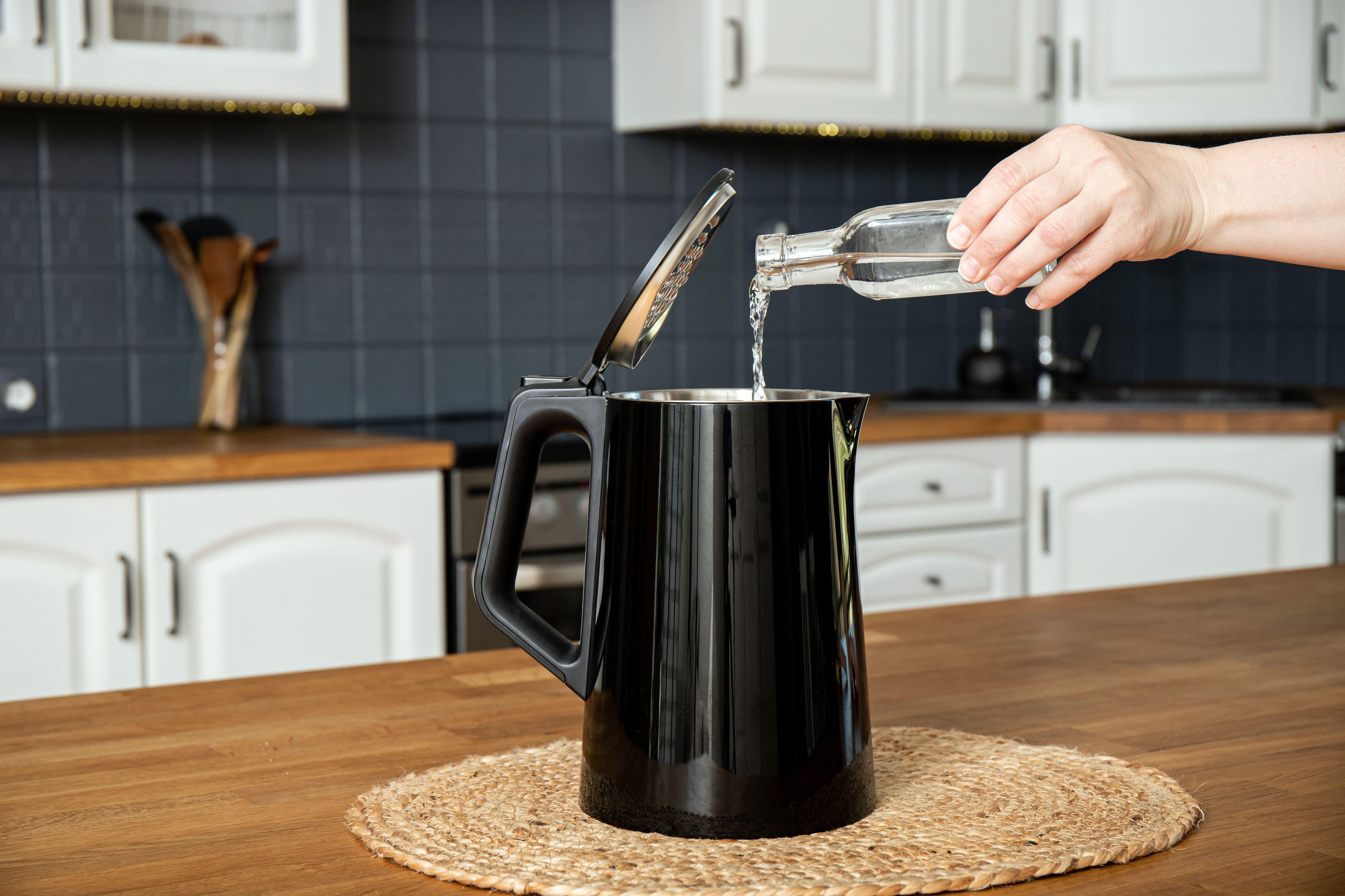 Woman pouring natural distilled acid white vinegar in electric kettle to remove boil away the limescale