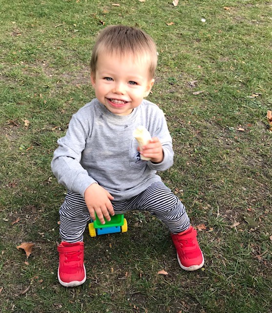 Toddler Frank Hanson sitting on a toy and holding a banana