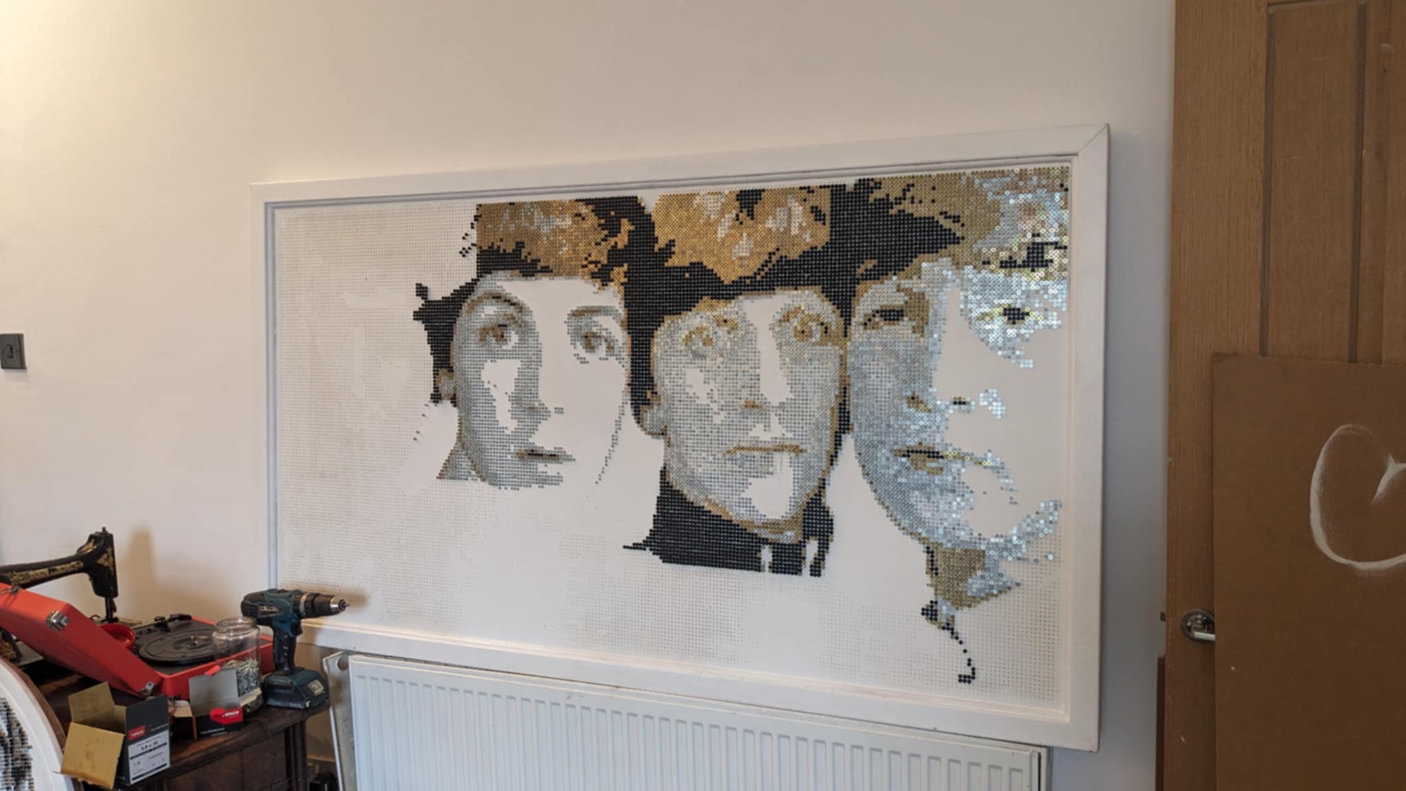 A partially completed artwork of The Beatles hanging on a wall