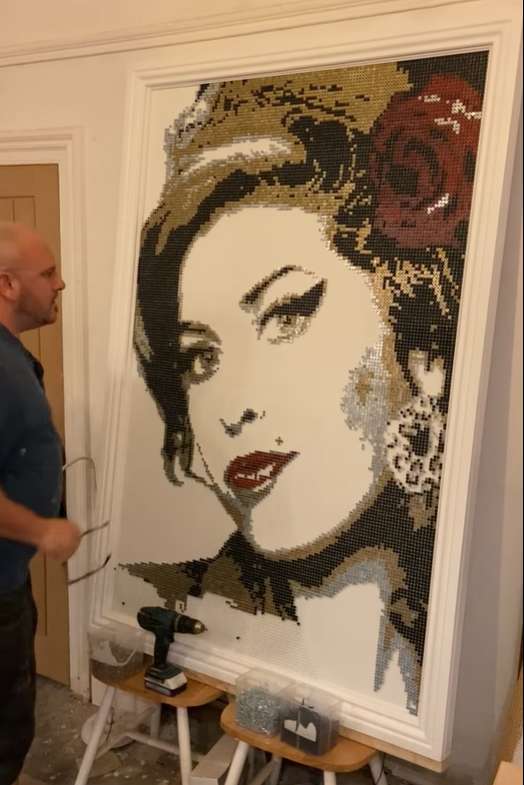 A man stands next to an artwork of Amy Winehouse made using screws