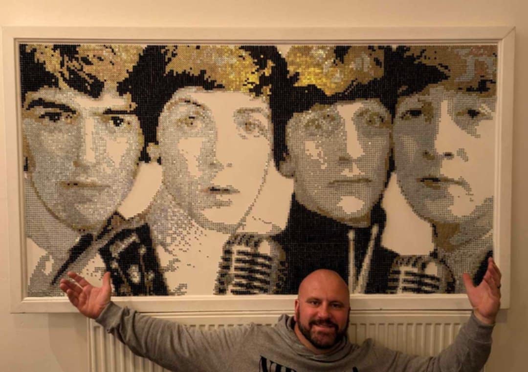 A man posing in front of an artwork of The Beatles