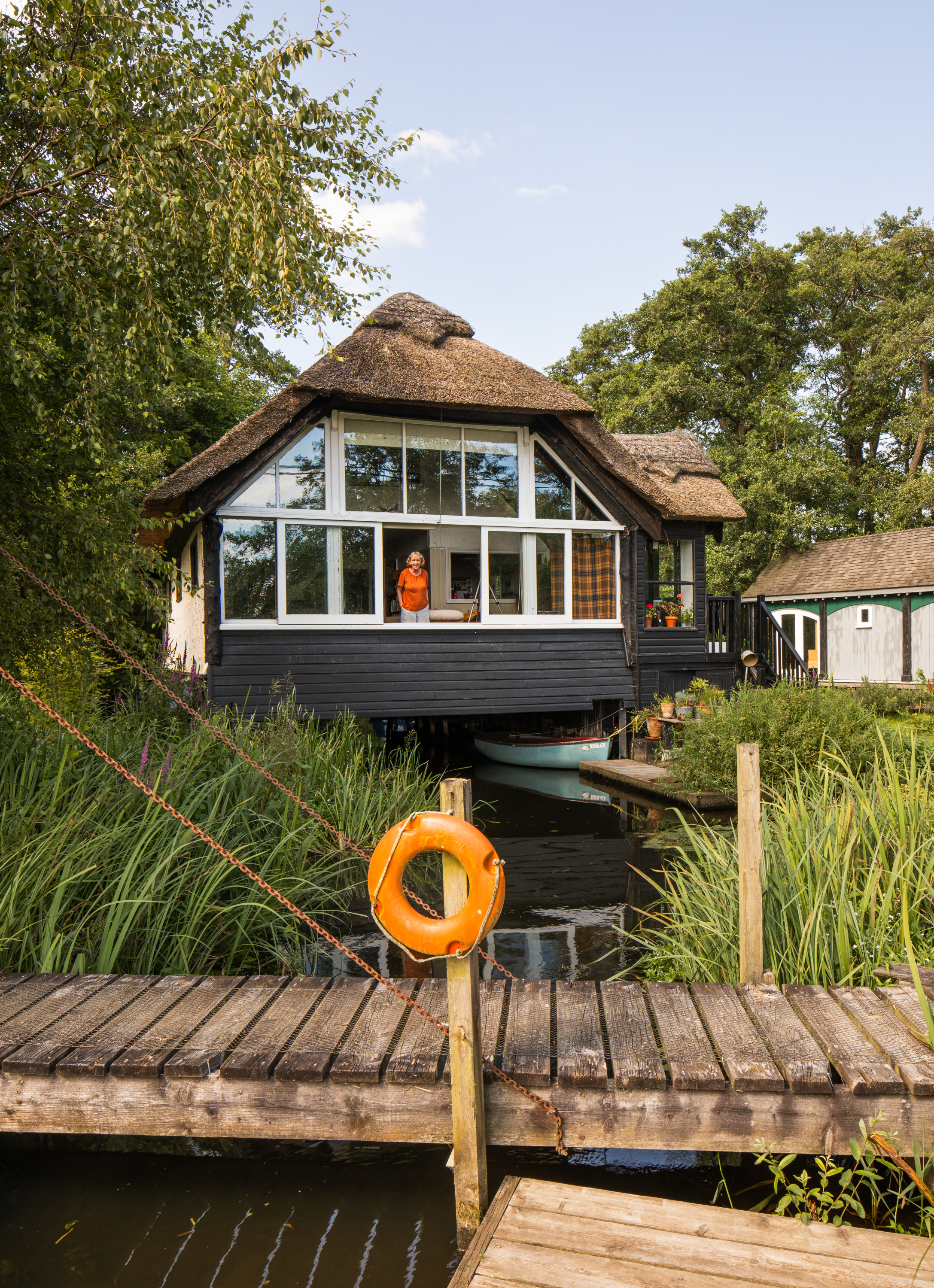 An exterior view of the thatched building Staithcote in Wroxham, Norfolk, with a woman looking out at the scene 