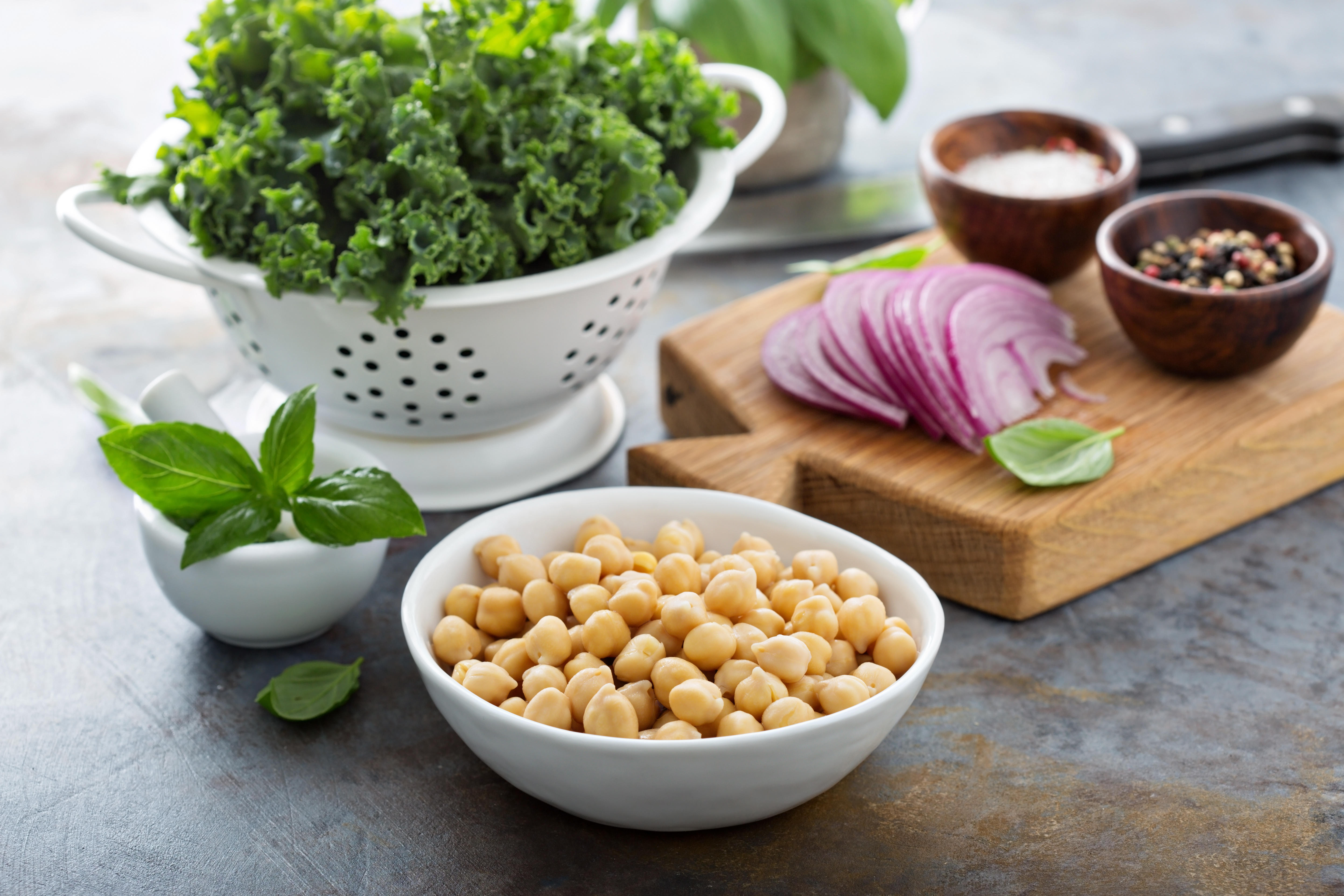 A bowl of chickpeas next to a colander of kale 