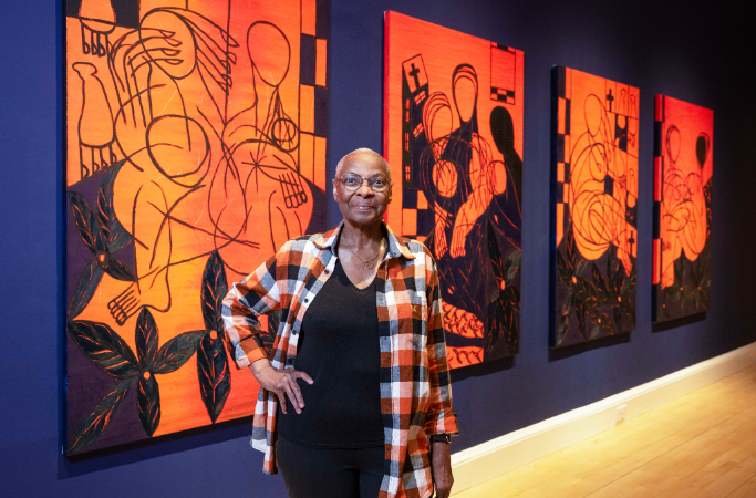 Everlyn Nicodemus standing in front of a row of her paintings