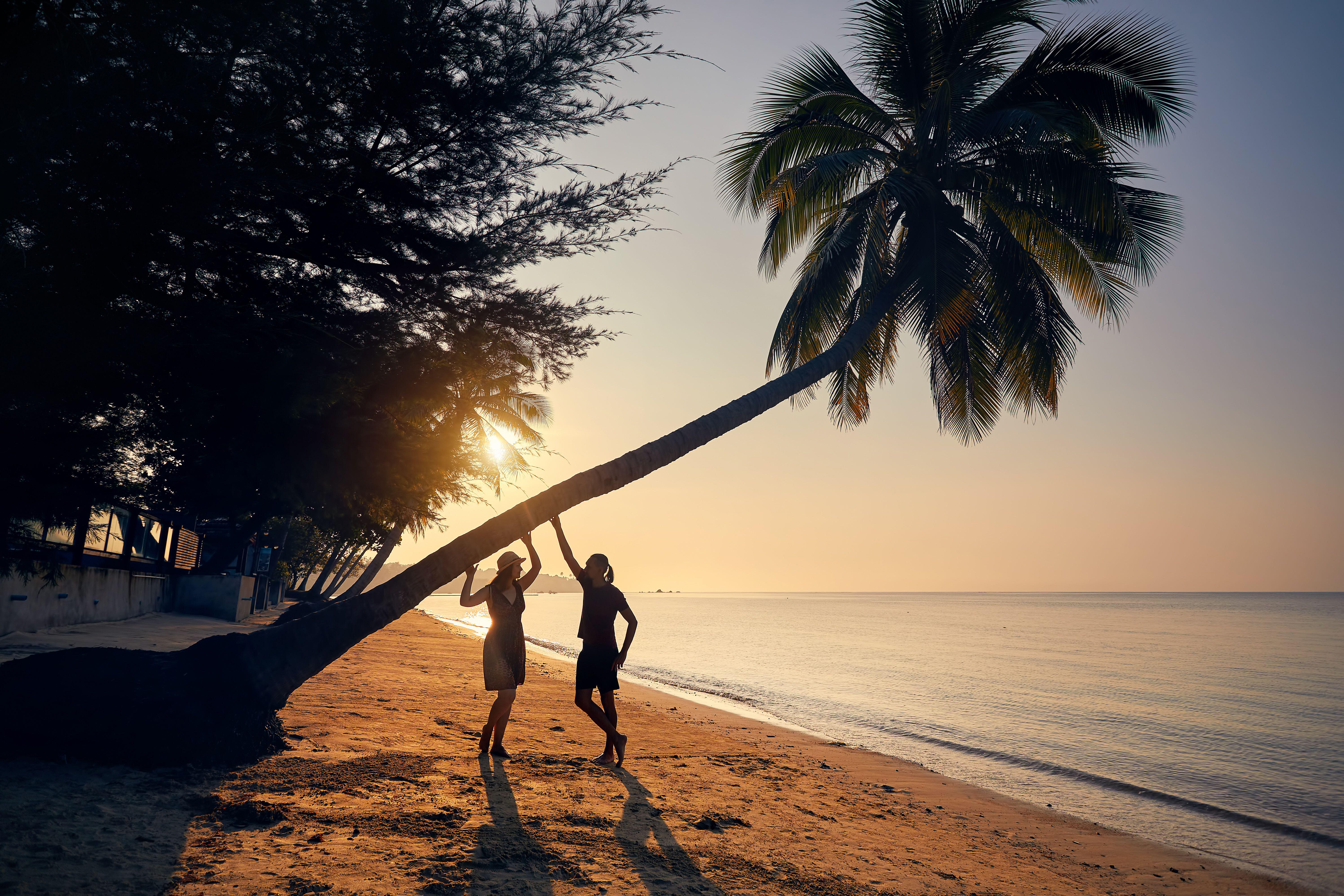 Happy couple in silhouette on the tropical beach near palm tree of Phi Phi island in Southern Thailand. Travel magazine vacation concept.