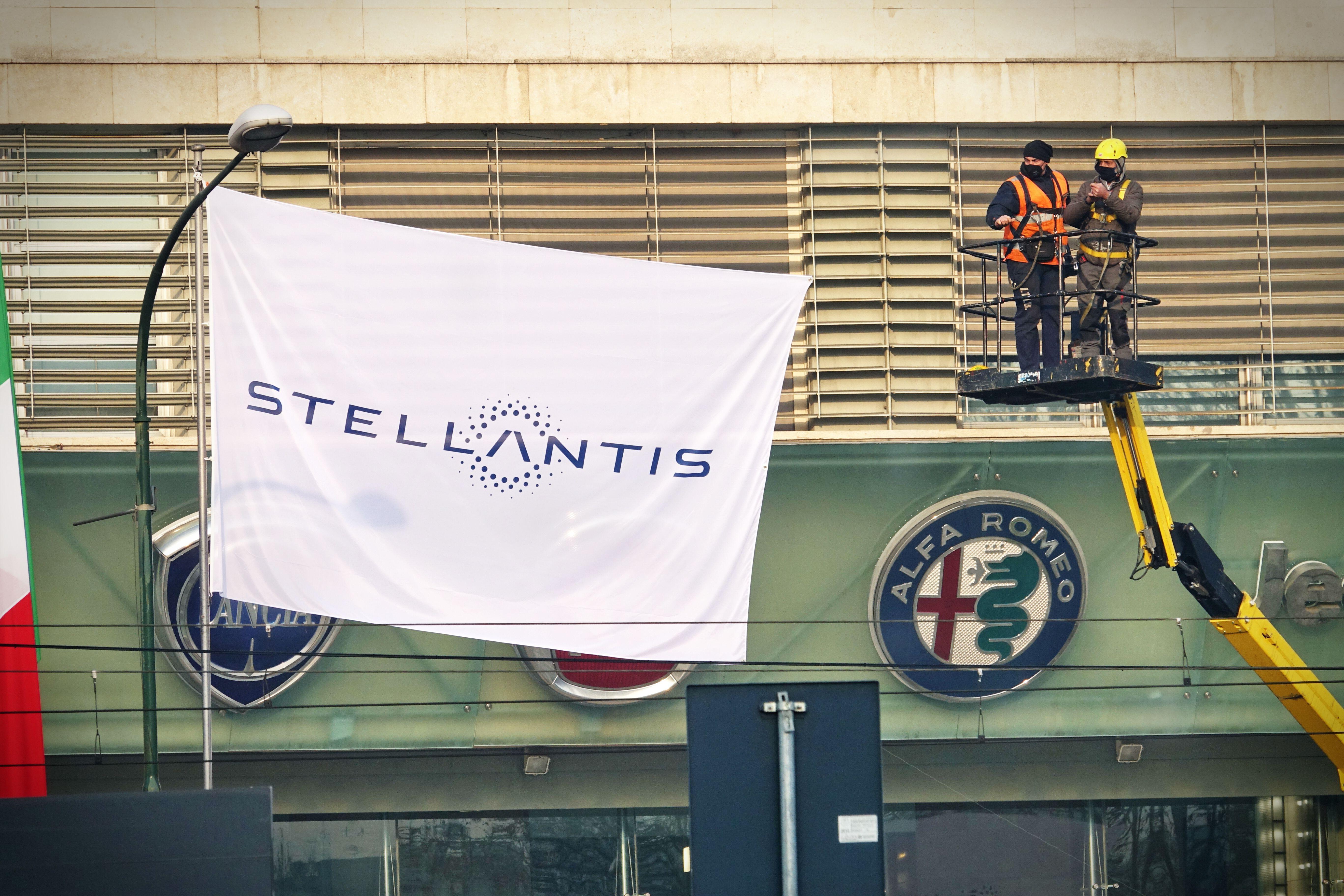 Workers next to a Stellantis flag and an Alfa Romeo sign 