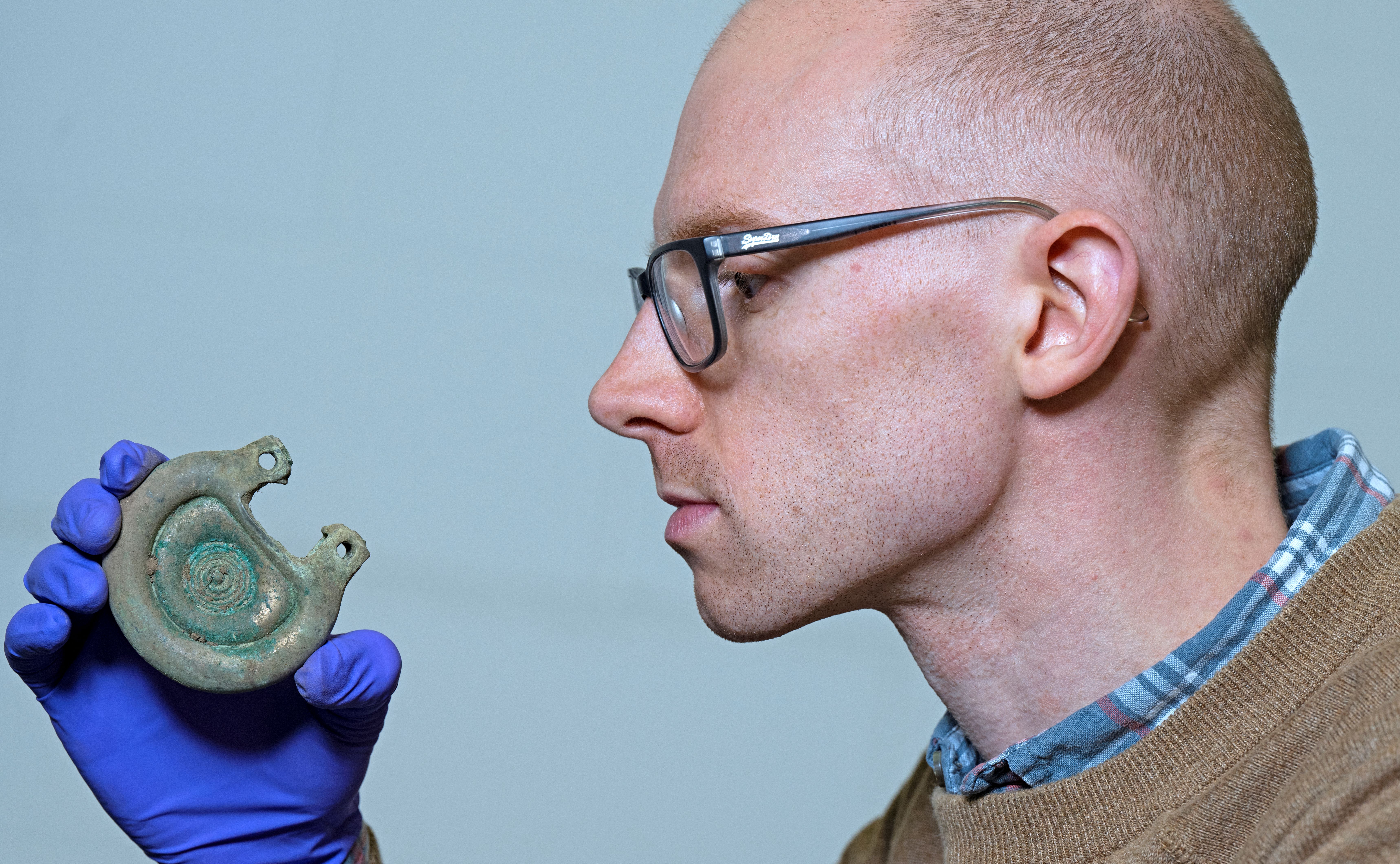 Side-on photo of Dr Matthew Knight looking at a bronze object from the Peebles Hoard