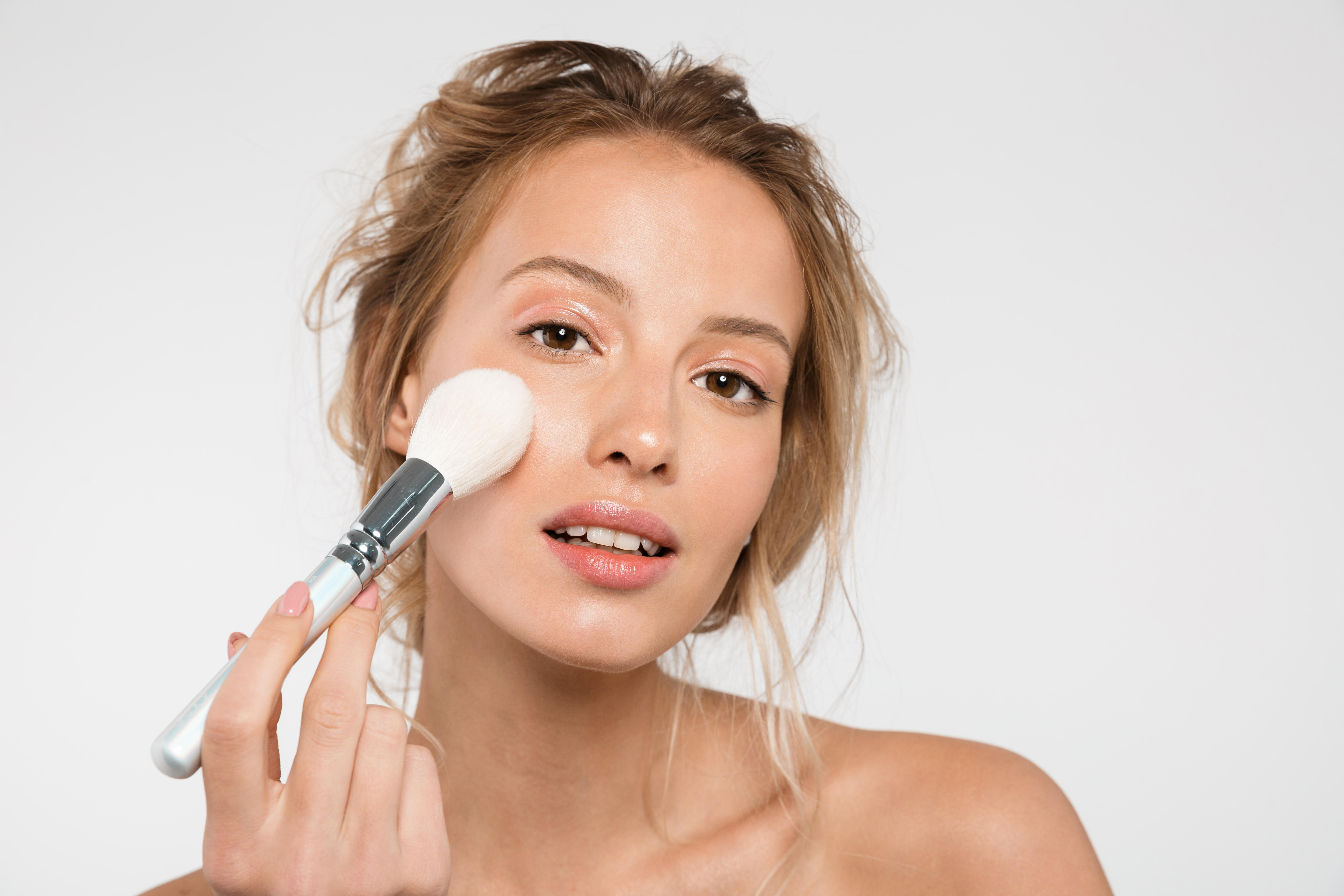 Young woman applies make-up with big fluffy brush