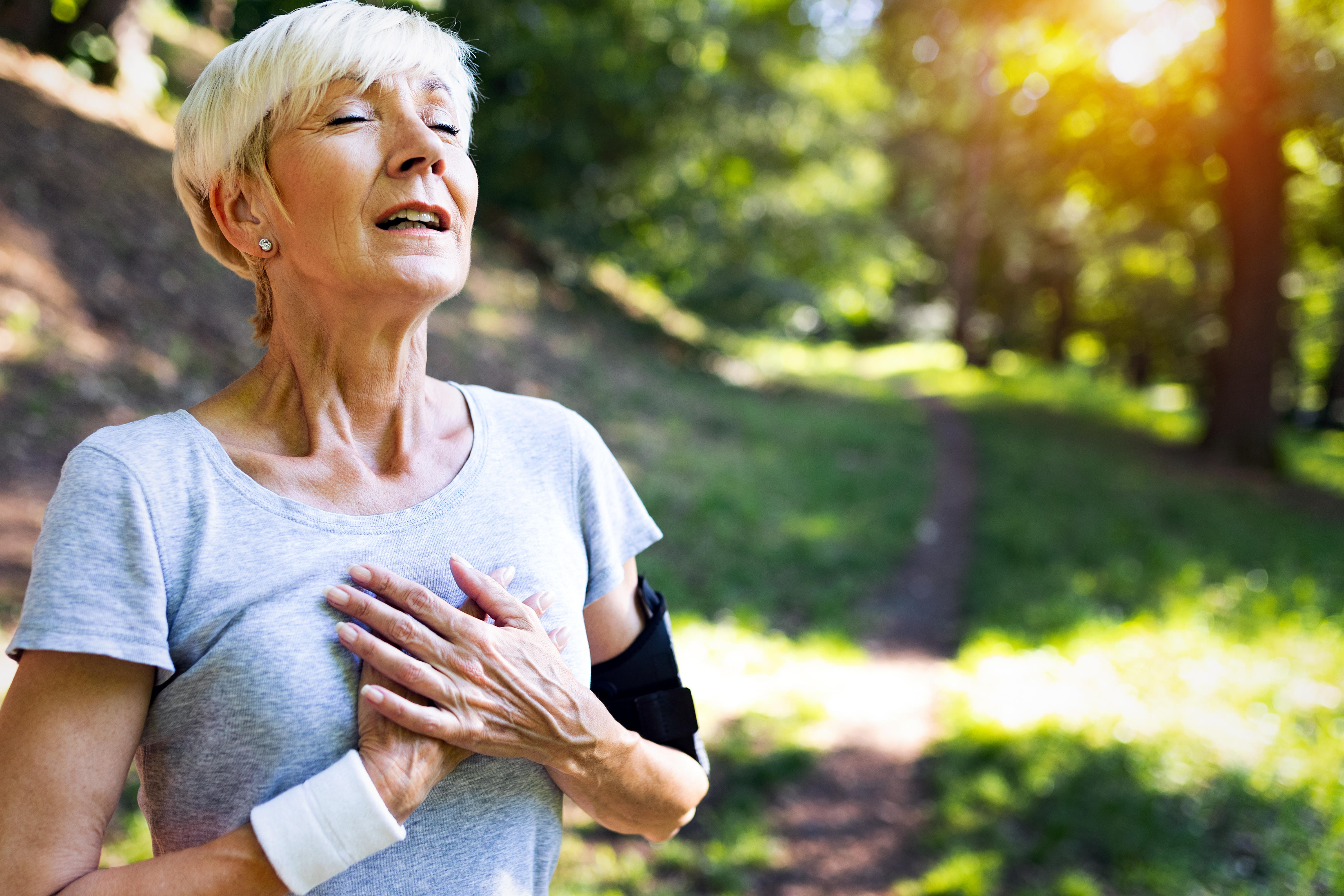 A senior woman experiencing chest pains after a run in a park