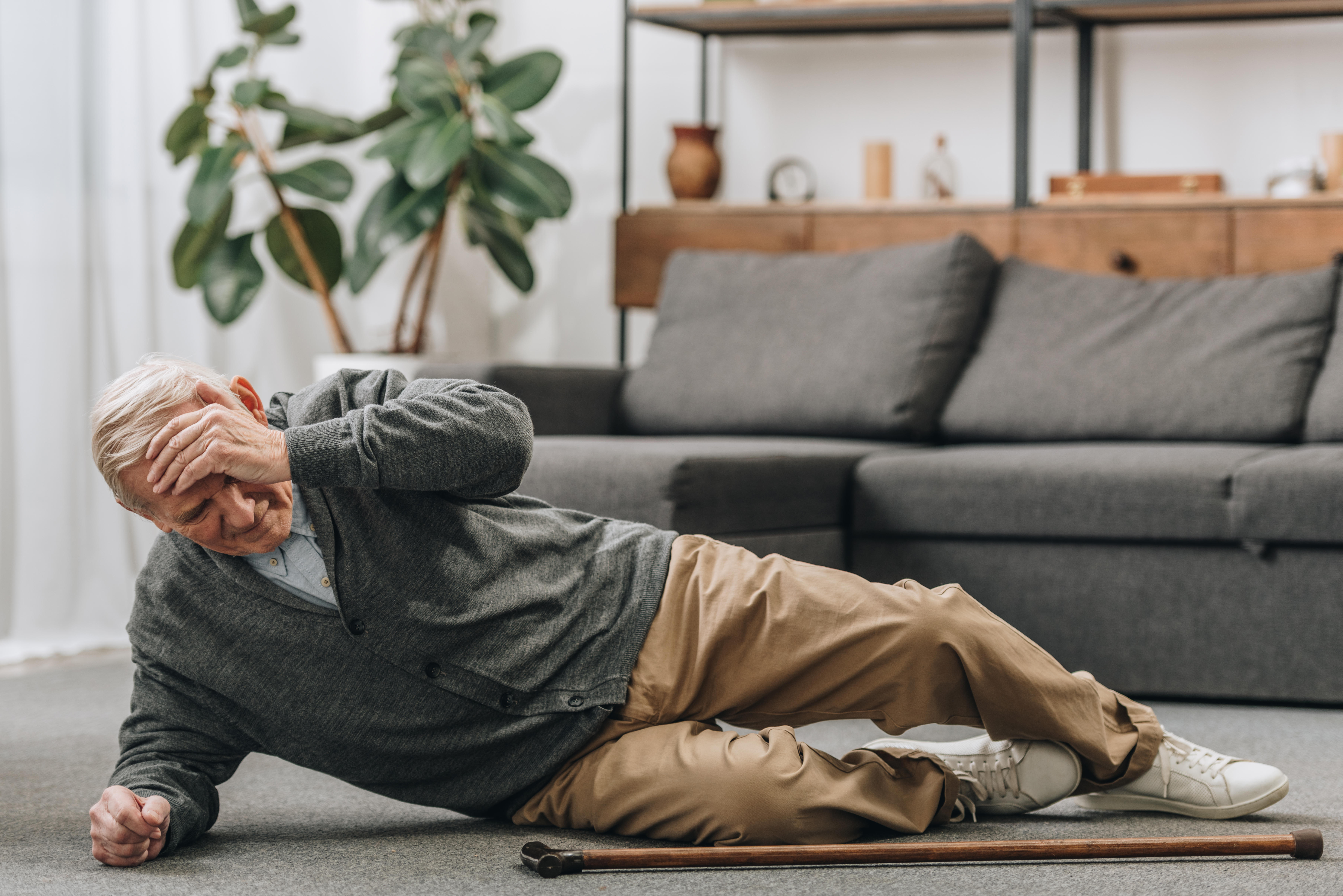 Old man laying on the floor with his hand on his forehead 