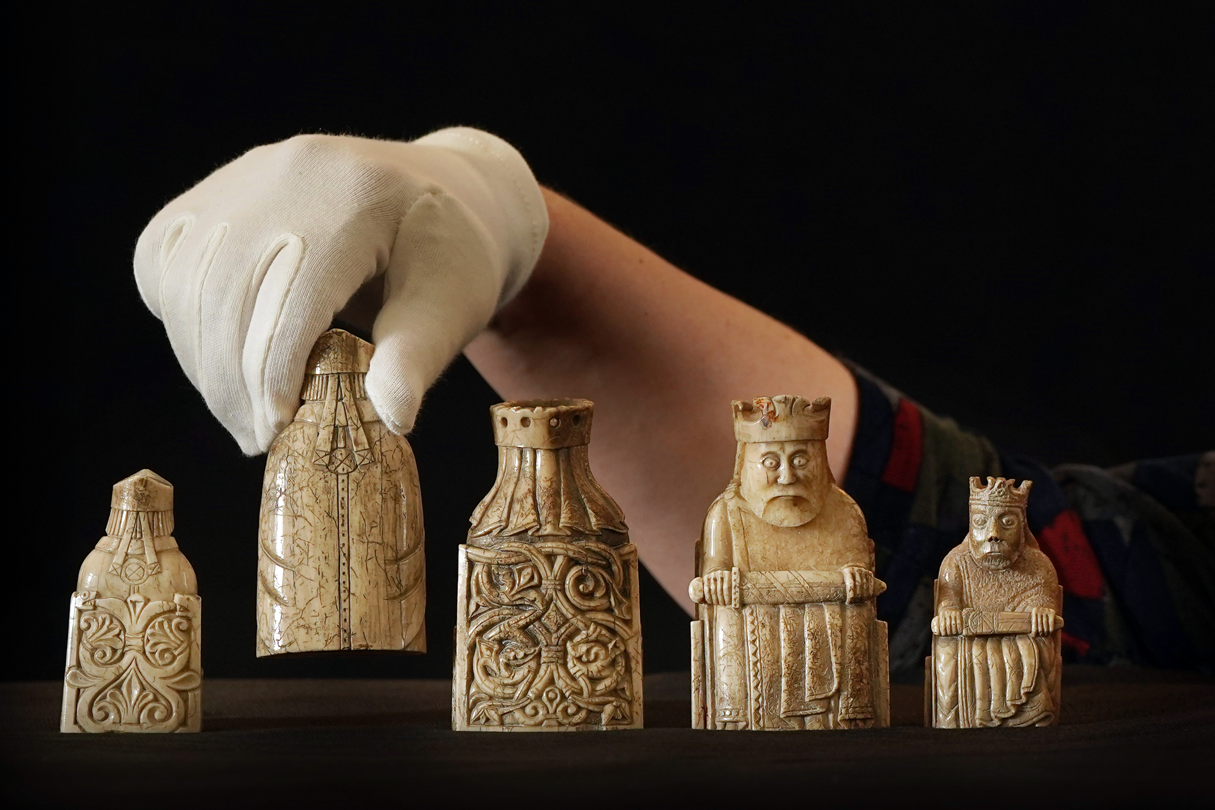 Five Lewis chessmen, with one being held up by a gloved hand