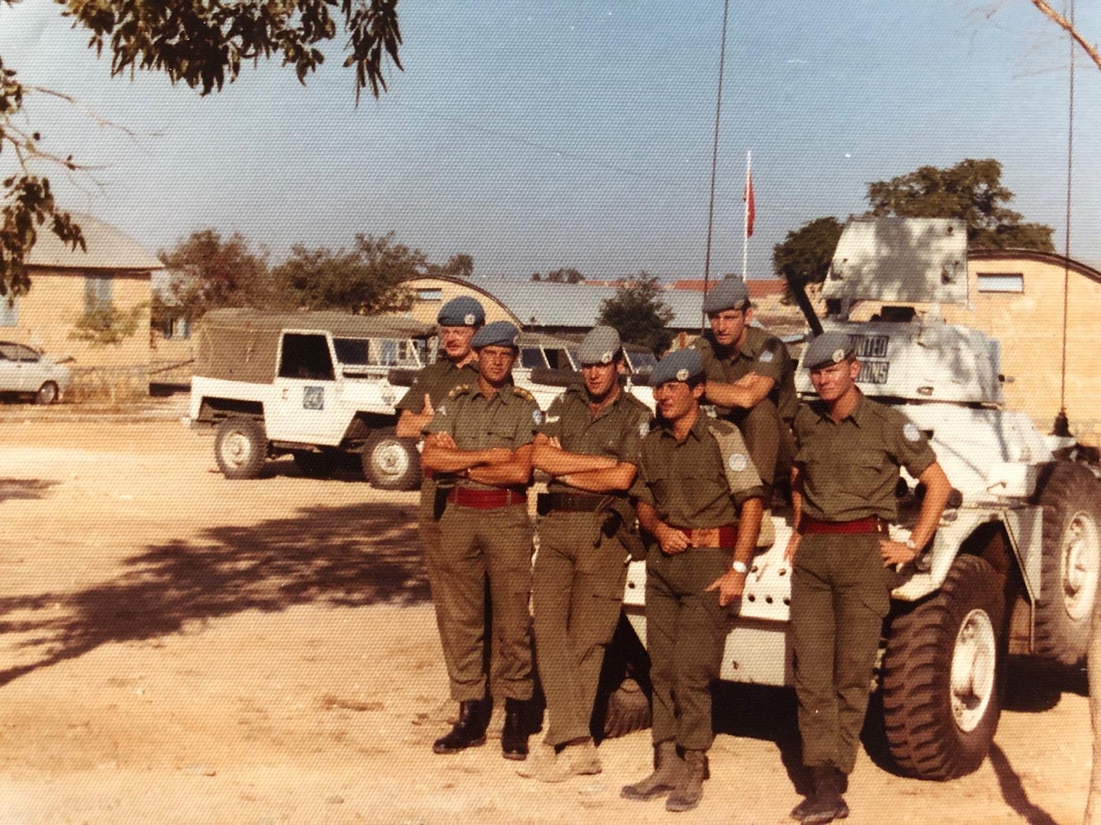 Group of soldiers standing in front of a white UN Peacekeeping vehicle in a sunny location