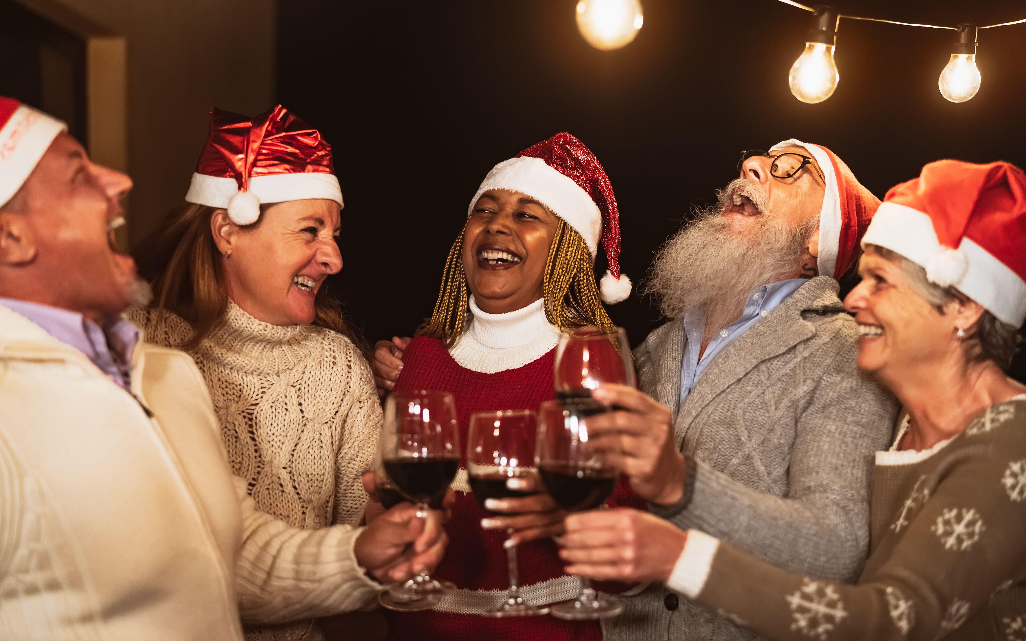 Happy senior friends celebrating Christmas holidays while toasting with red wine glasses on house patio party