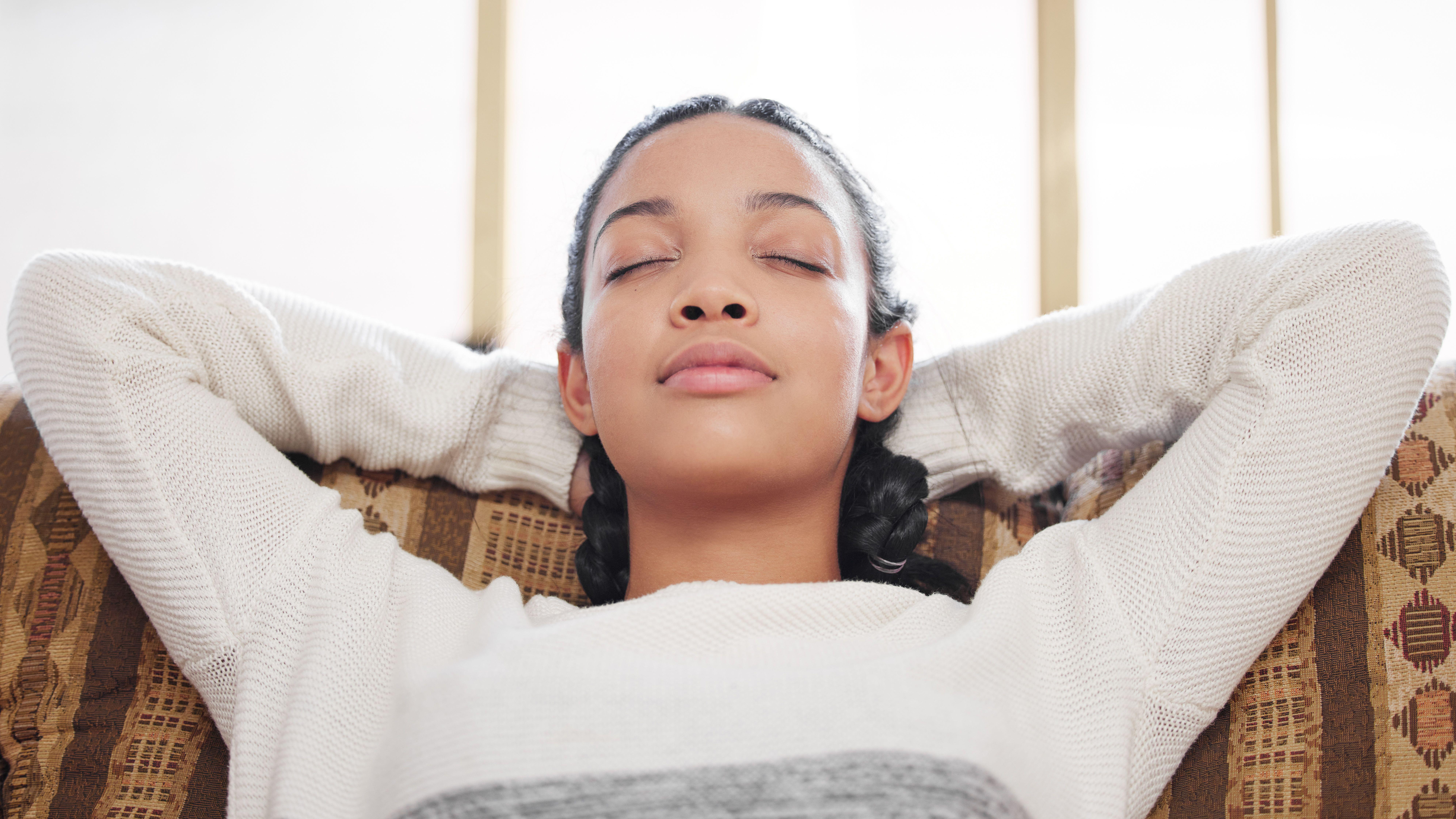 Young woman closing her eyes and relaxing on the sofa at home 