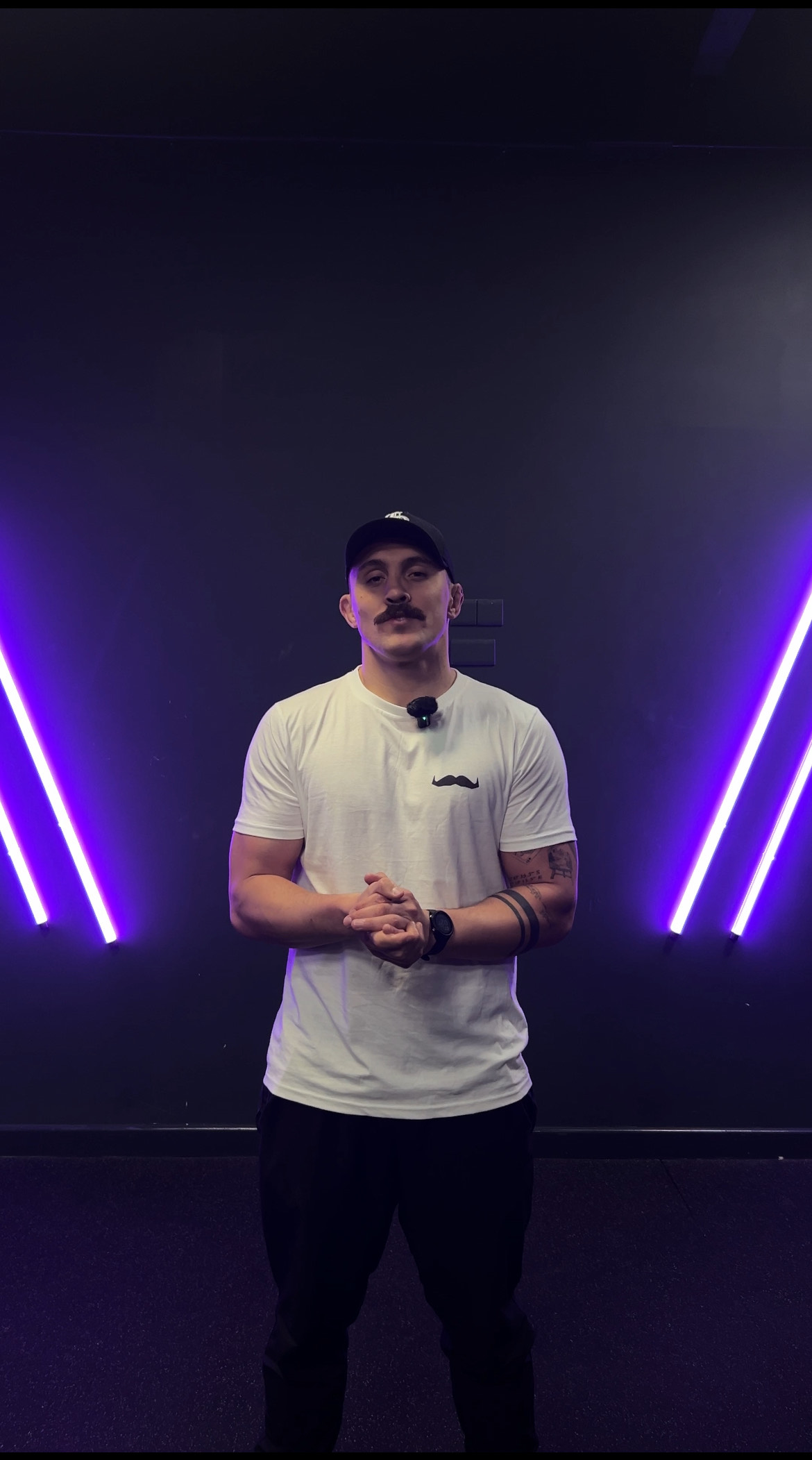 Man wearing white t-shirt and black cap stands in front of purple lights