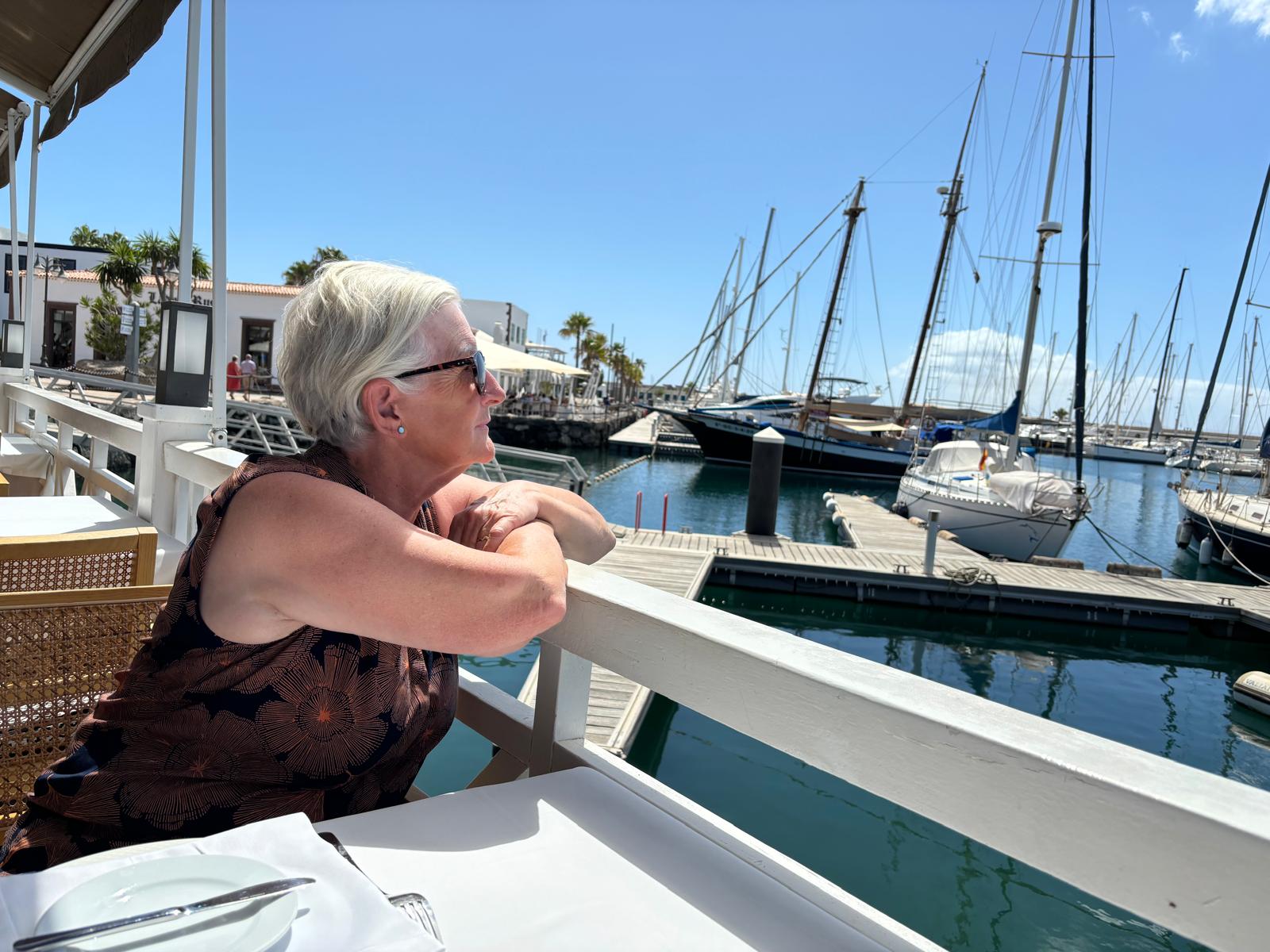 Julie sitting at a table turning to look out over a harbour 