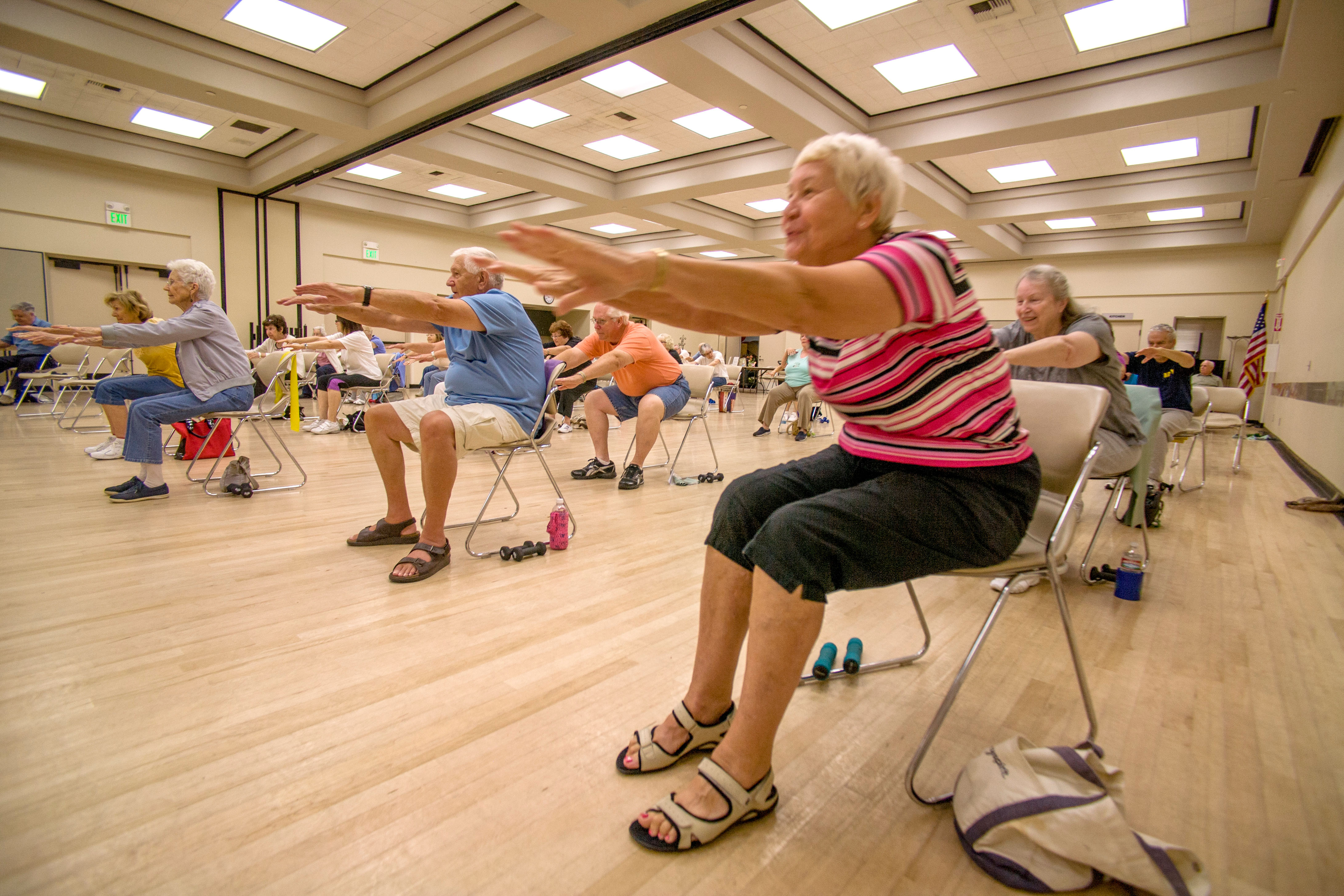 Senior group taking part in a chair exercise class in a sports hall 