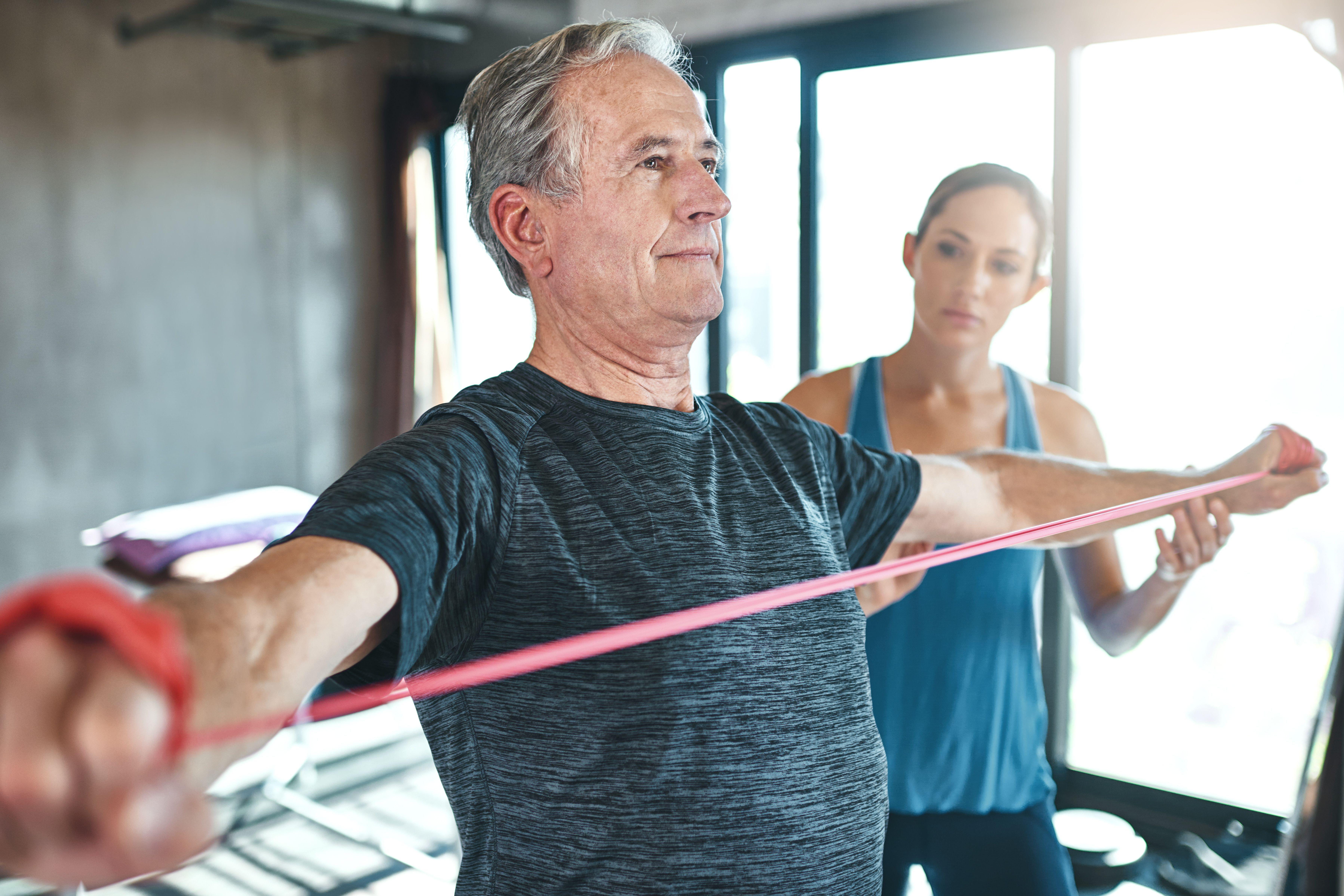 A middle aged man using a resistance band being coached by a female personal trainer 