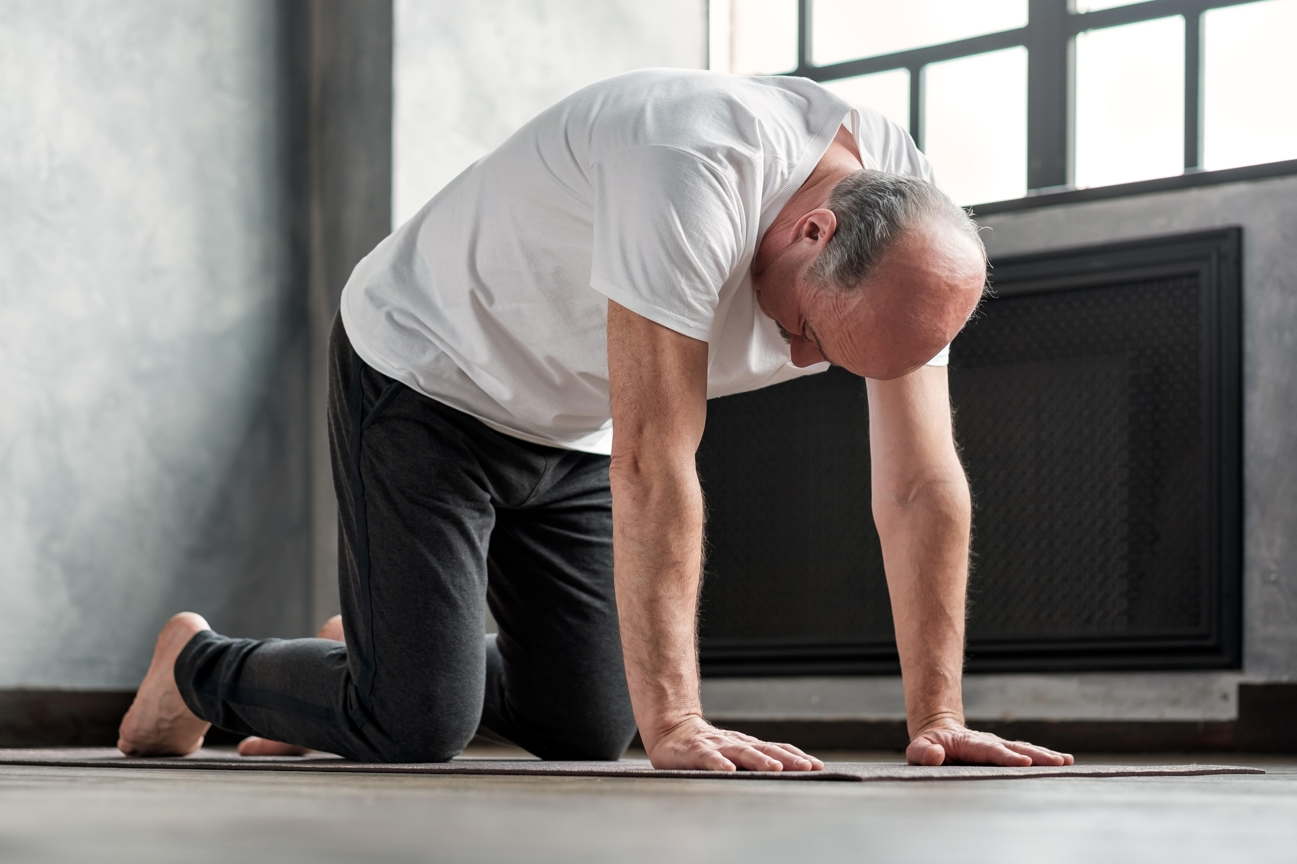 Senior man practicing the cat cow yoga poses on a yoga mat at home