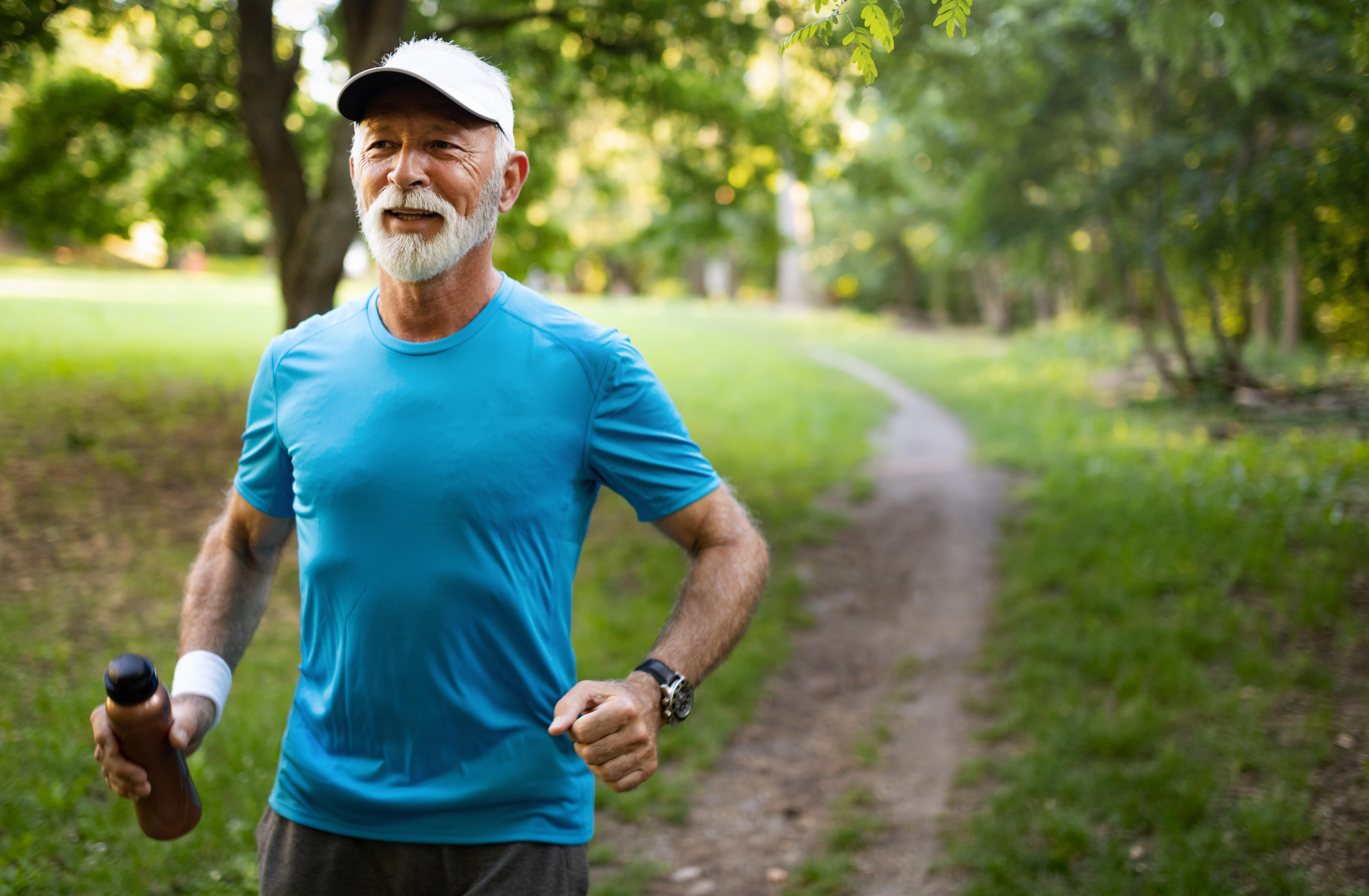 Retired man wearing blue top jogging through a park 