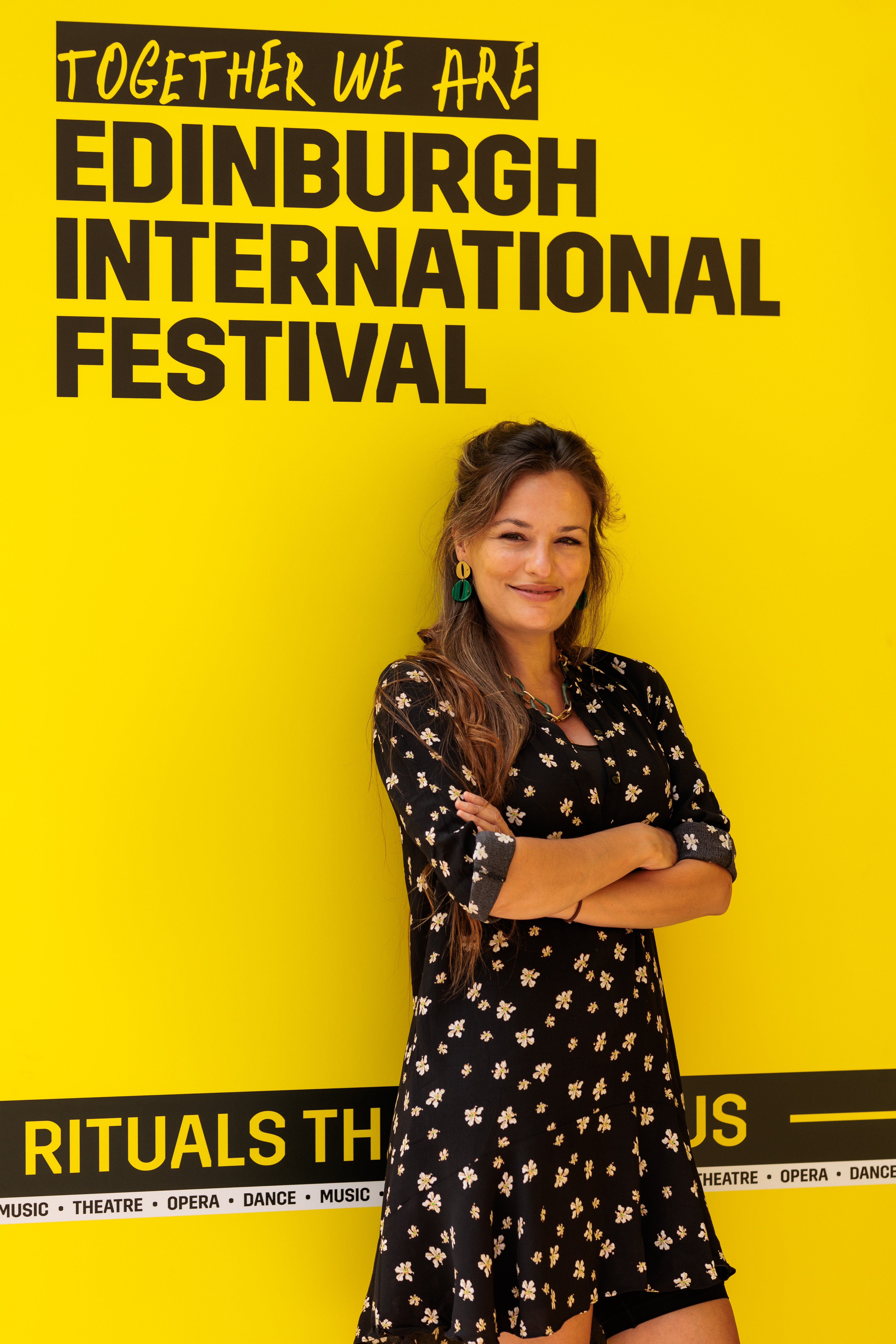 Nicola Benedetti standing with arms folded in front of an Edinburgh International Festival billboard