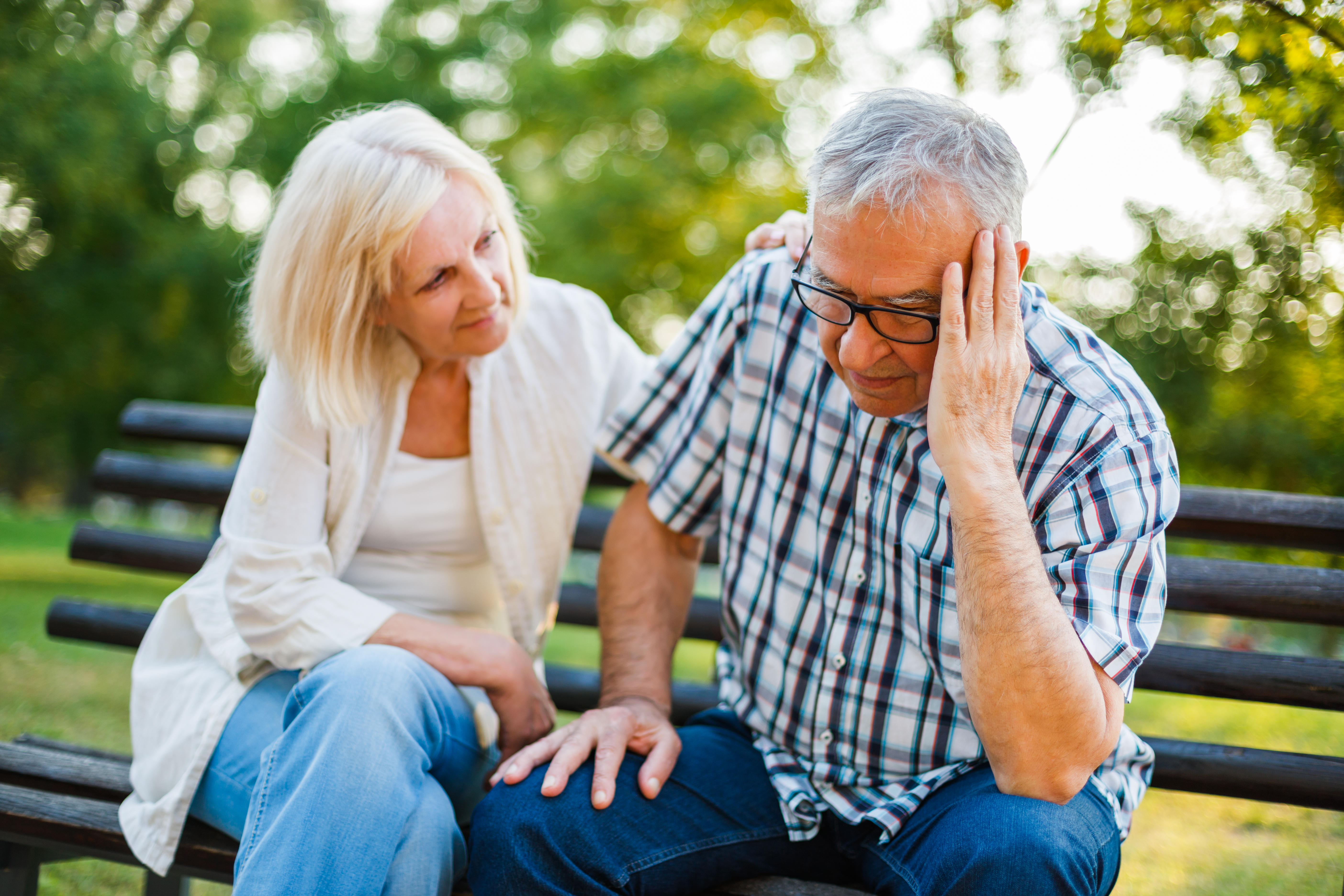 Senior lady consoling her depressed husband on a park bench