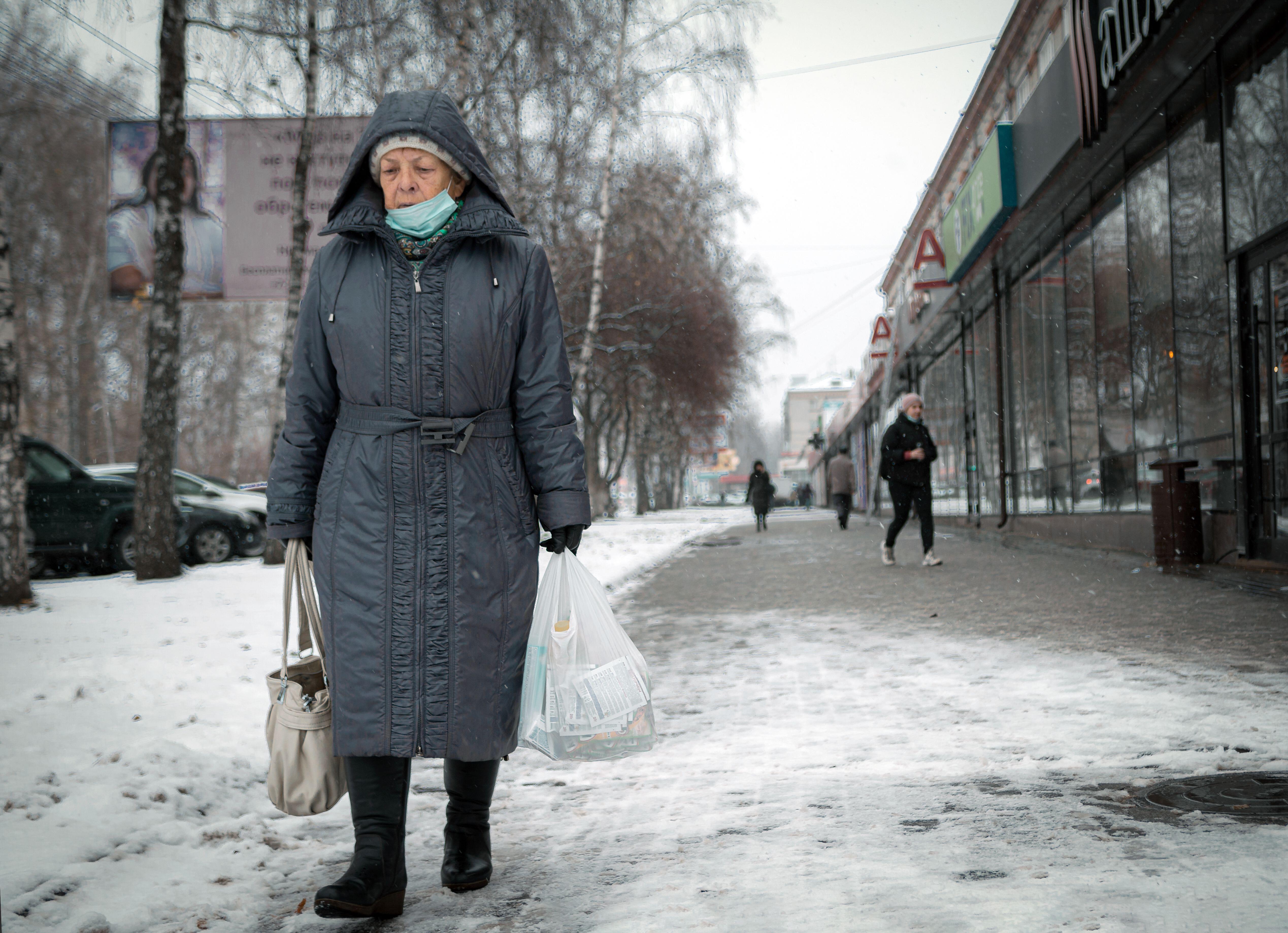 Older woman walking through snowy street with bags of shopping 