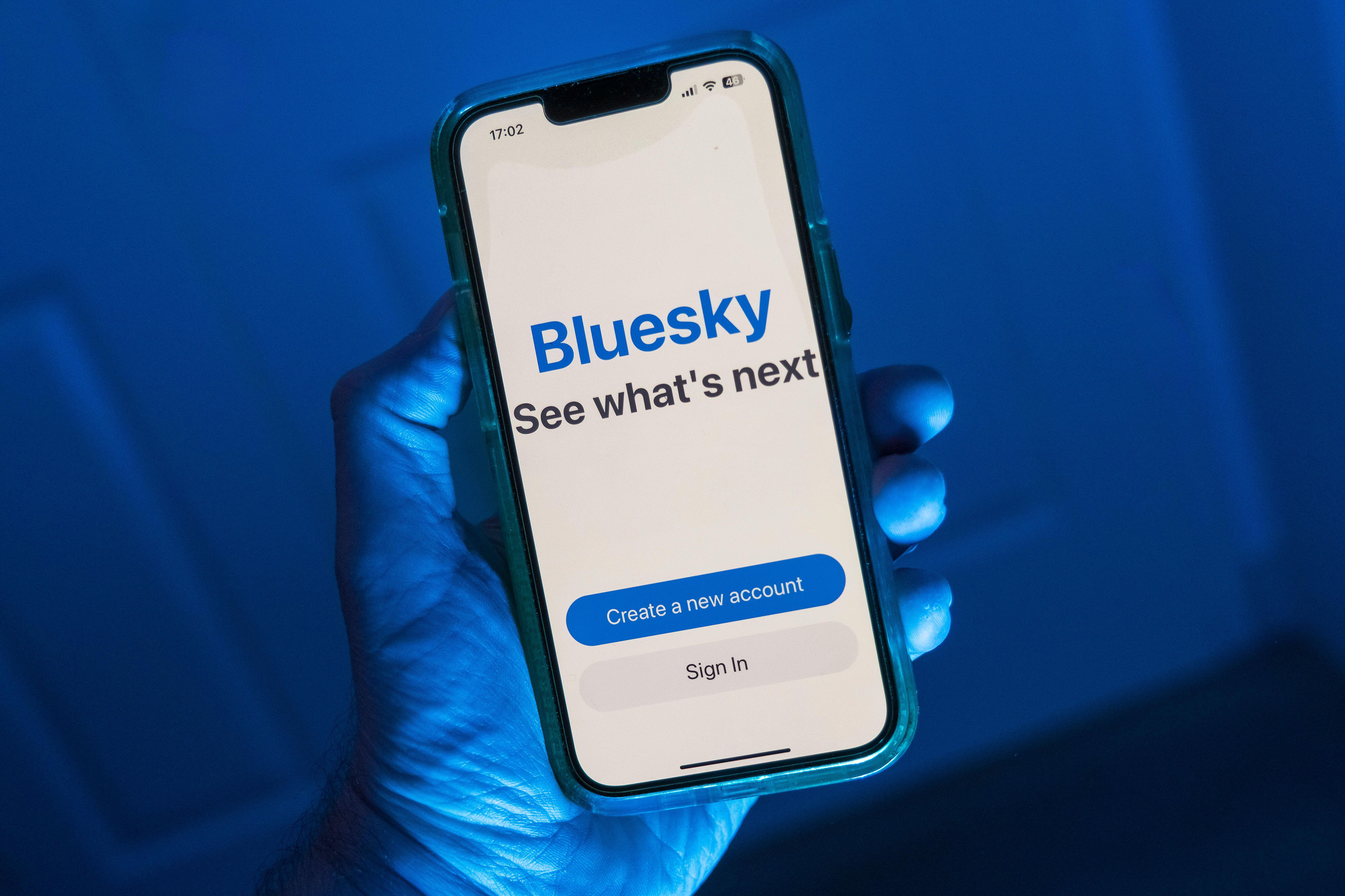 A hand holding an IPhone with the Bluesky app on it 