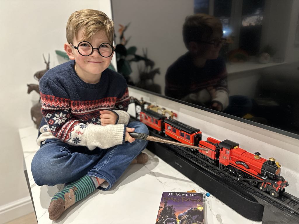 Boy in Harry Potter glasses, pointing his wand at a model of the Hogwarts Express