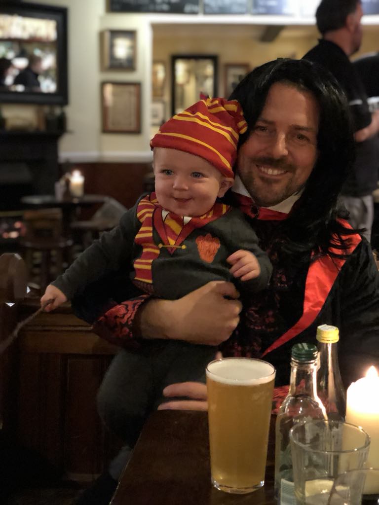 Baby dressed as Harry Potter smiling in the arms of his father, dressed as Severus Snape