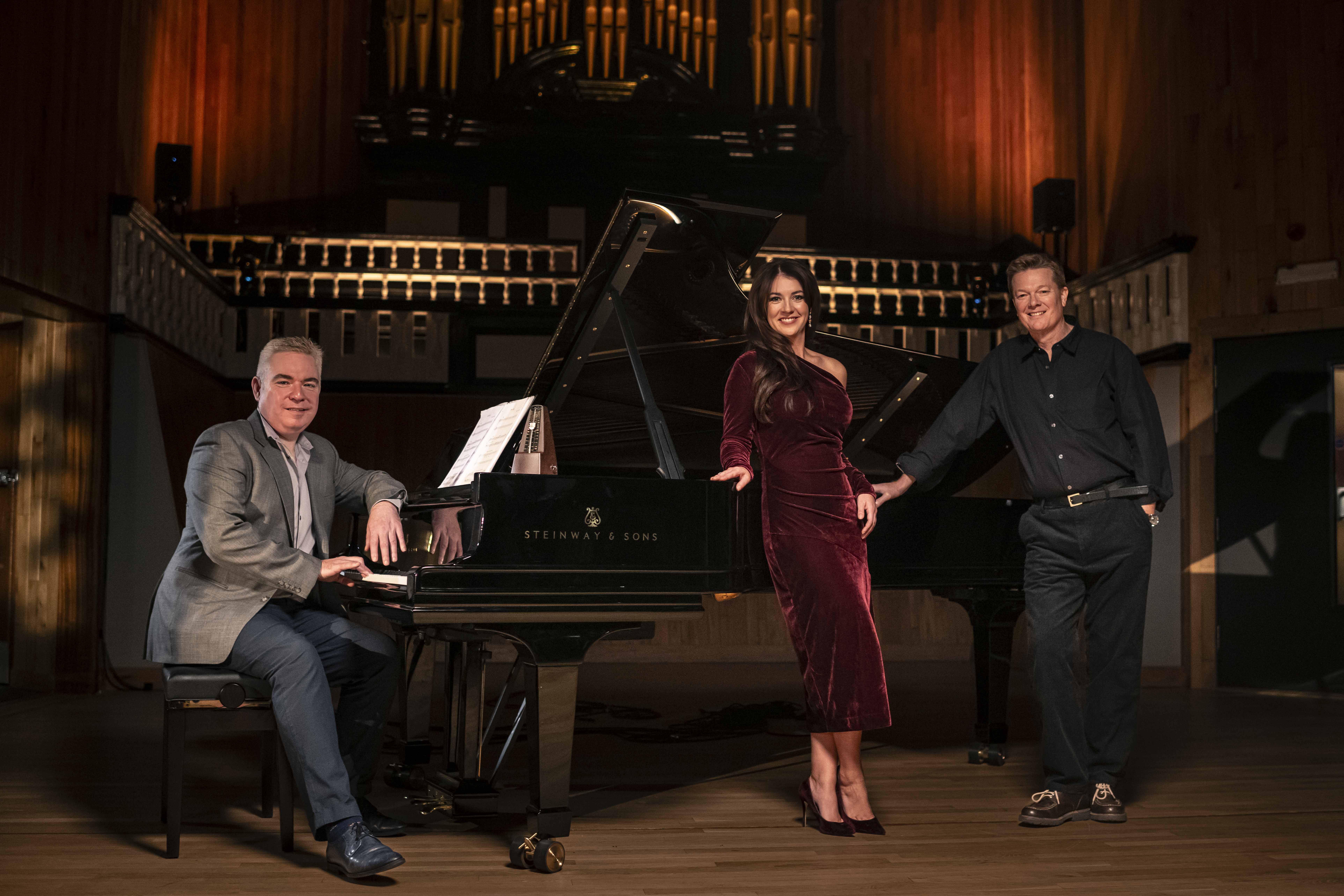 A woman and two men standing in front of  a piano