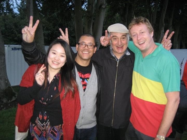 Ashley Beedle smiling and flashing peace signs with a group of people