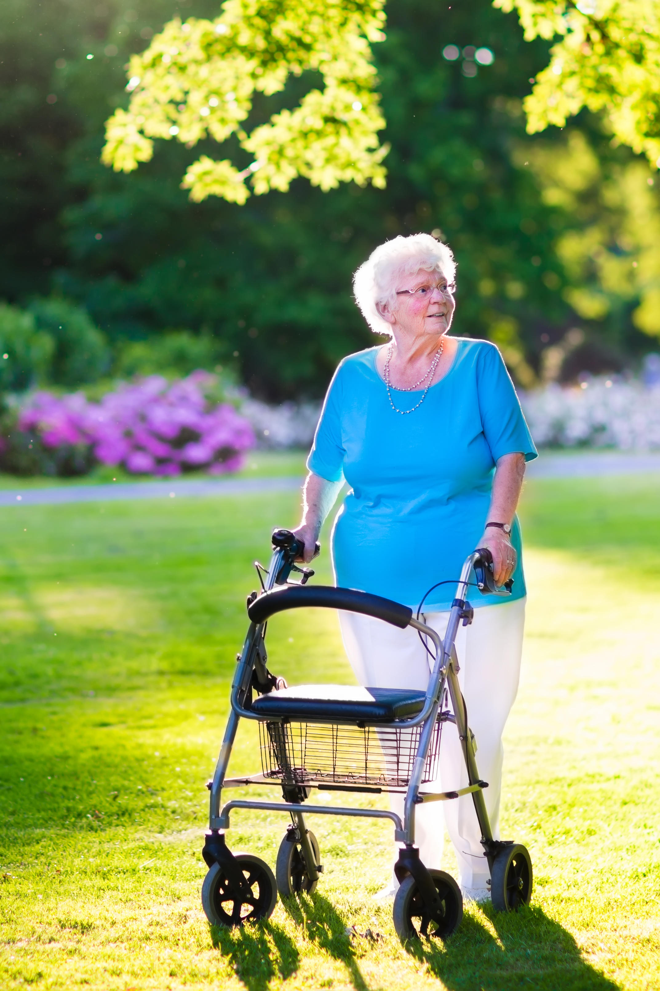 Happy retired senior lady with walking disability enjoying a day in the park going for a walk outside with a walker