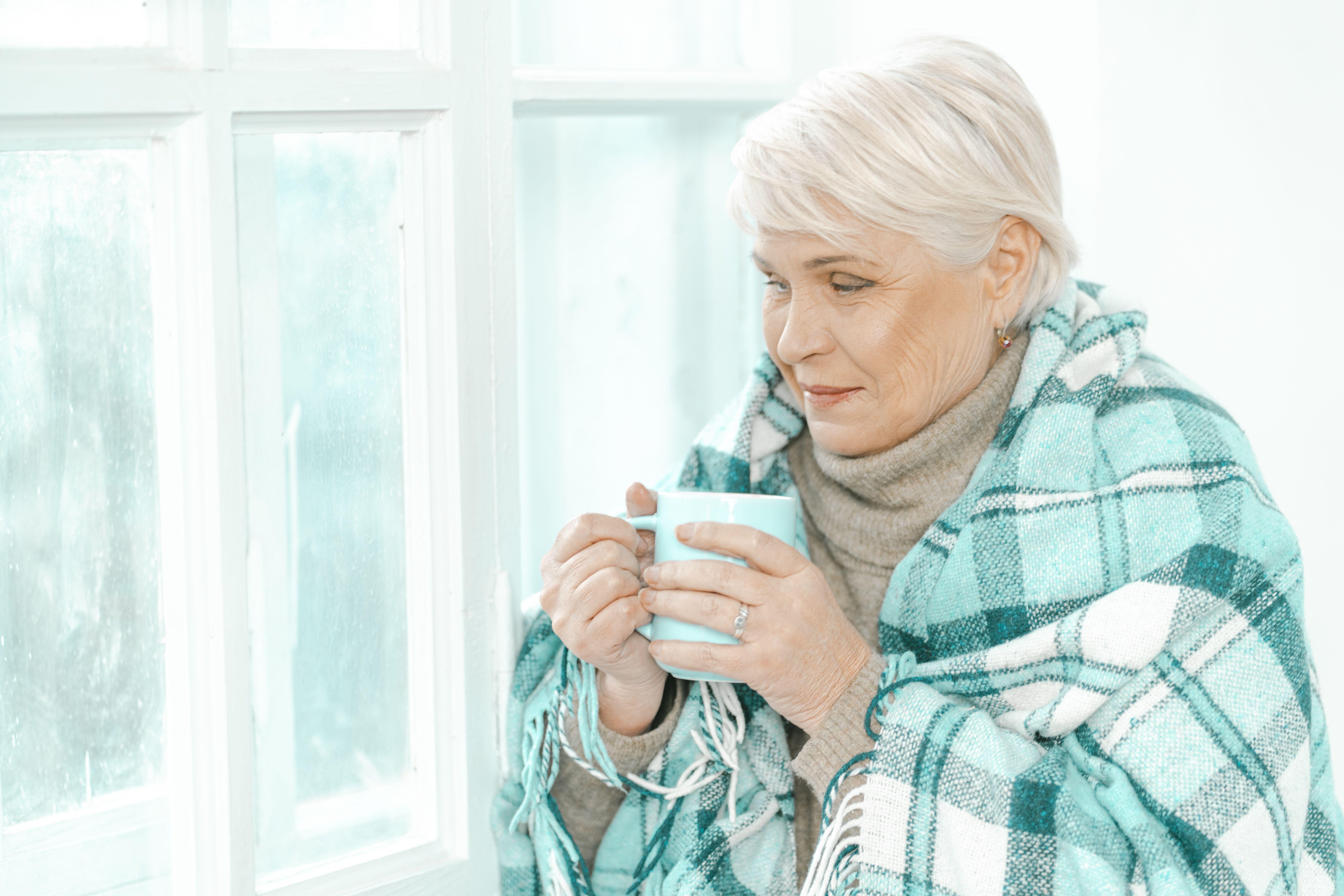 Senior woman wrapped in a blanket holding a mug of tea 