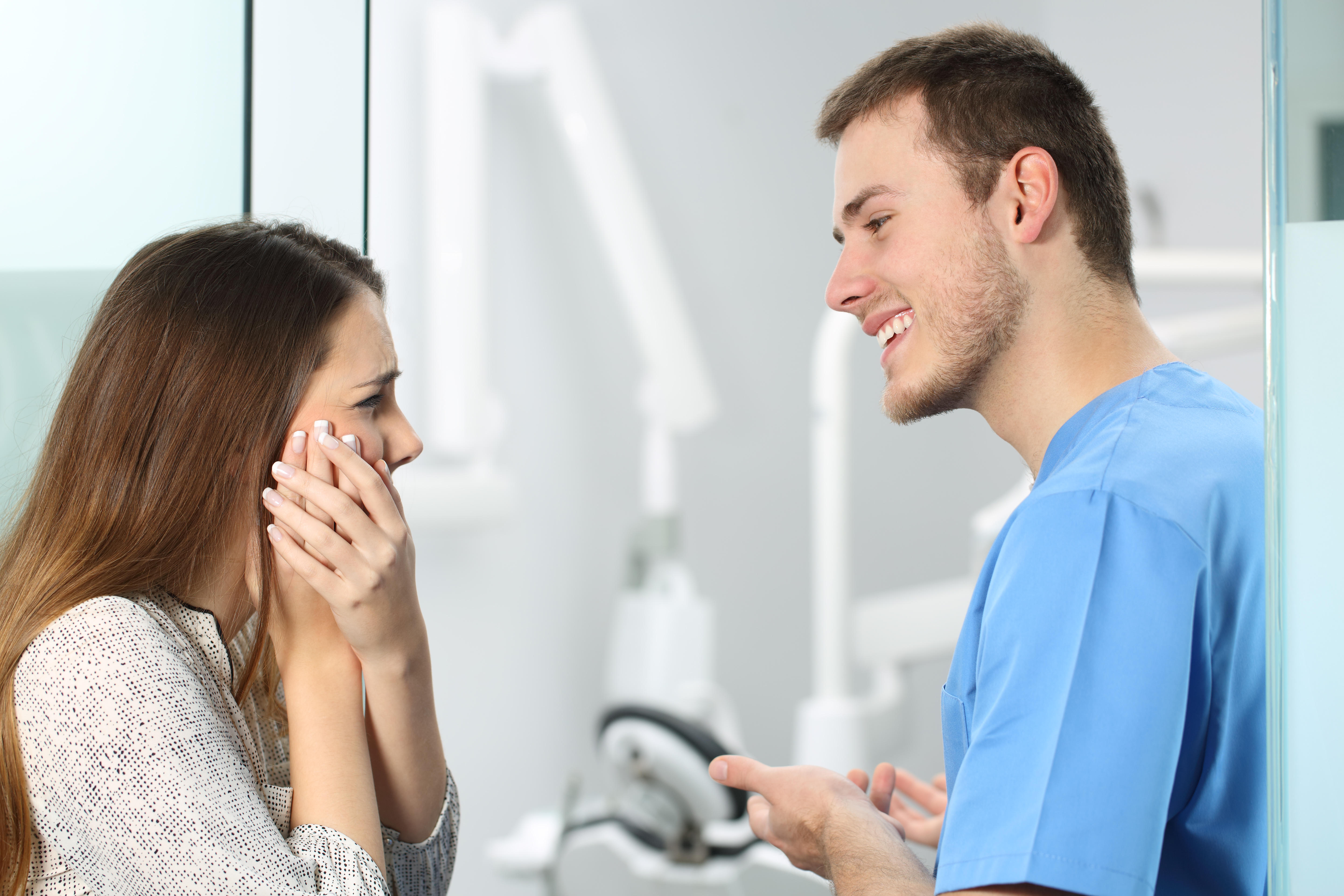 Male dentist talking to a female patient who is suffering from jaw ache 