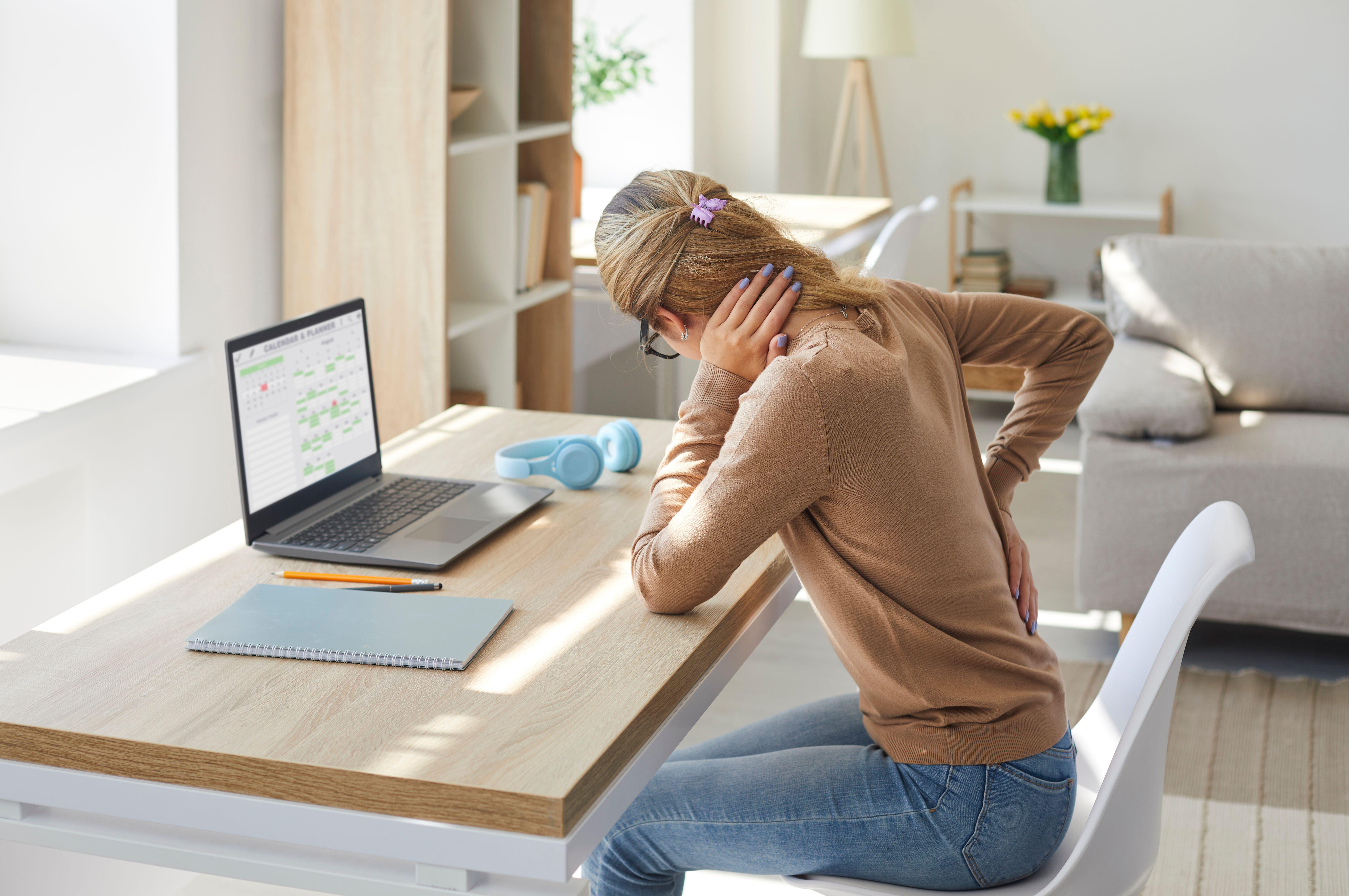 Woman working from home at a desk suffering from neck and back pain