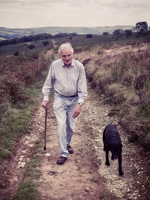 Captain Godsal walking in the countryside with a black dog next to him