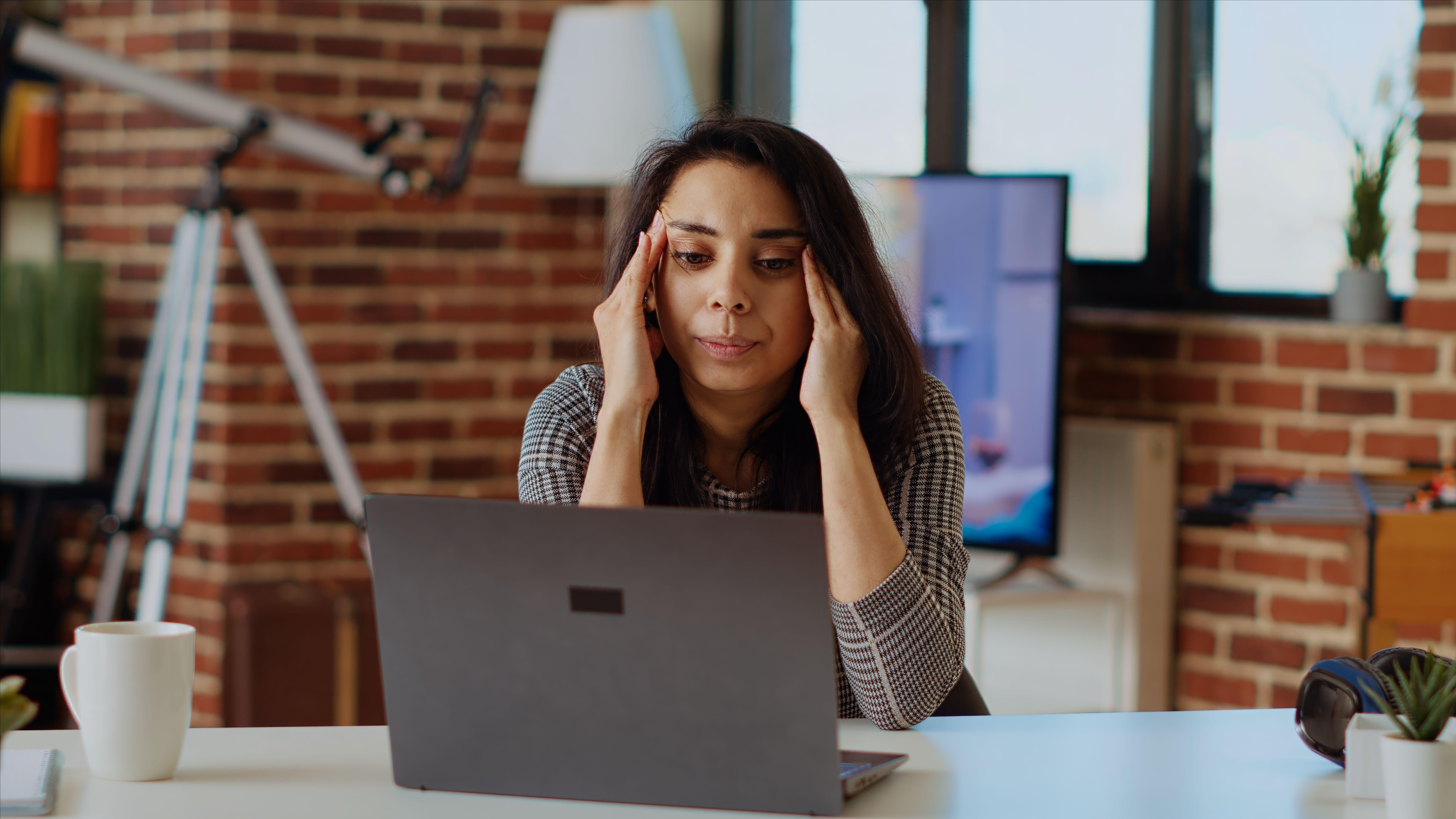 A woman sat at a desk with a laptop open struggling to concentrate 