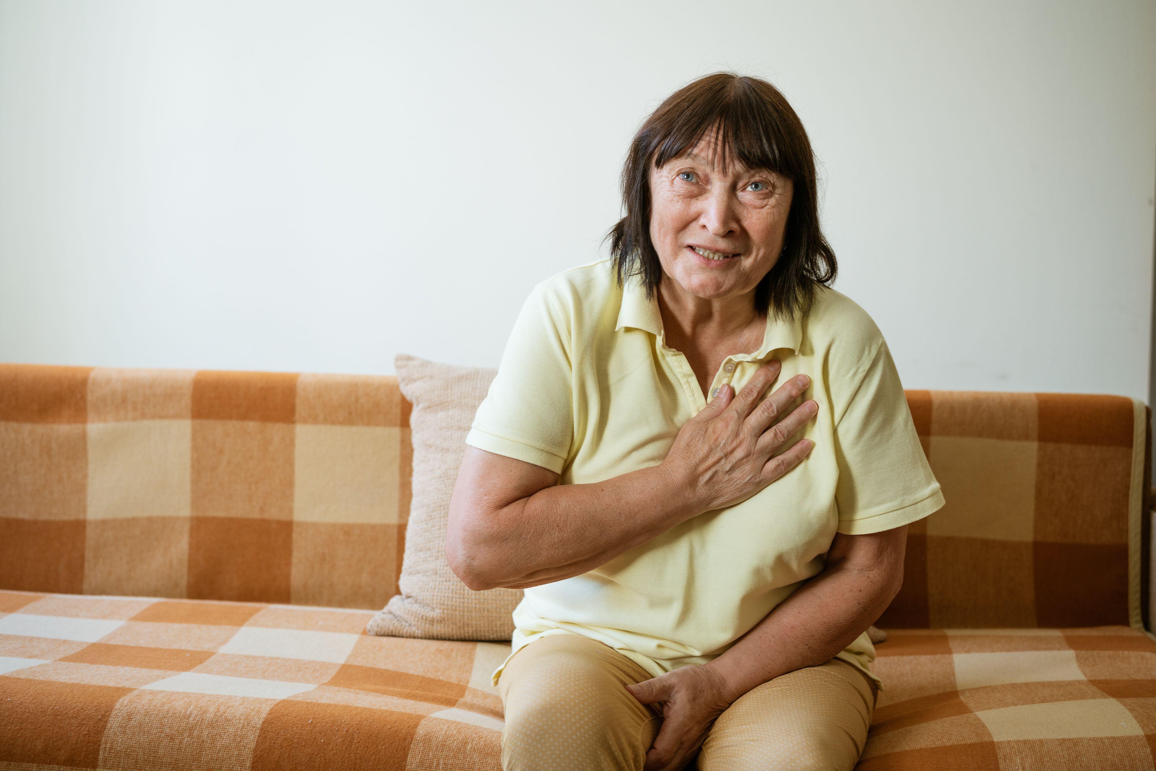 Mature woman sat on a sofa experiencing heart pains