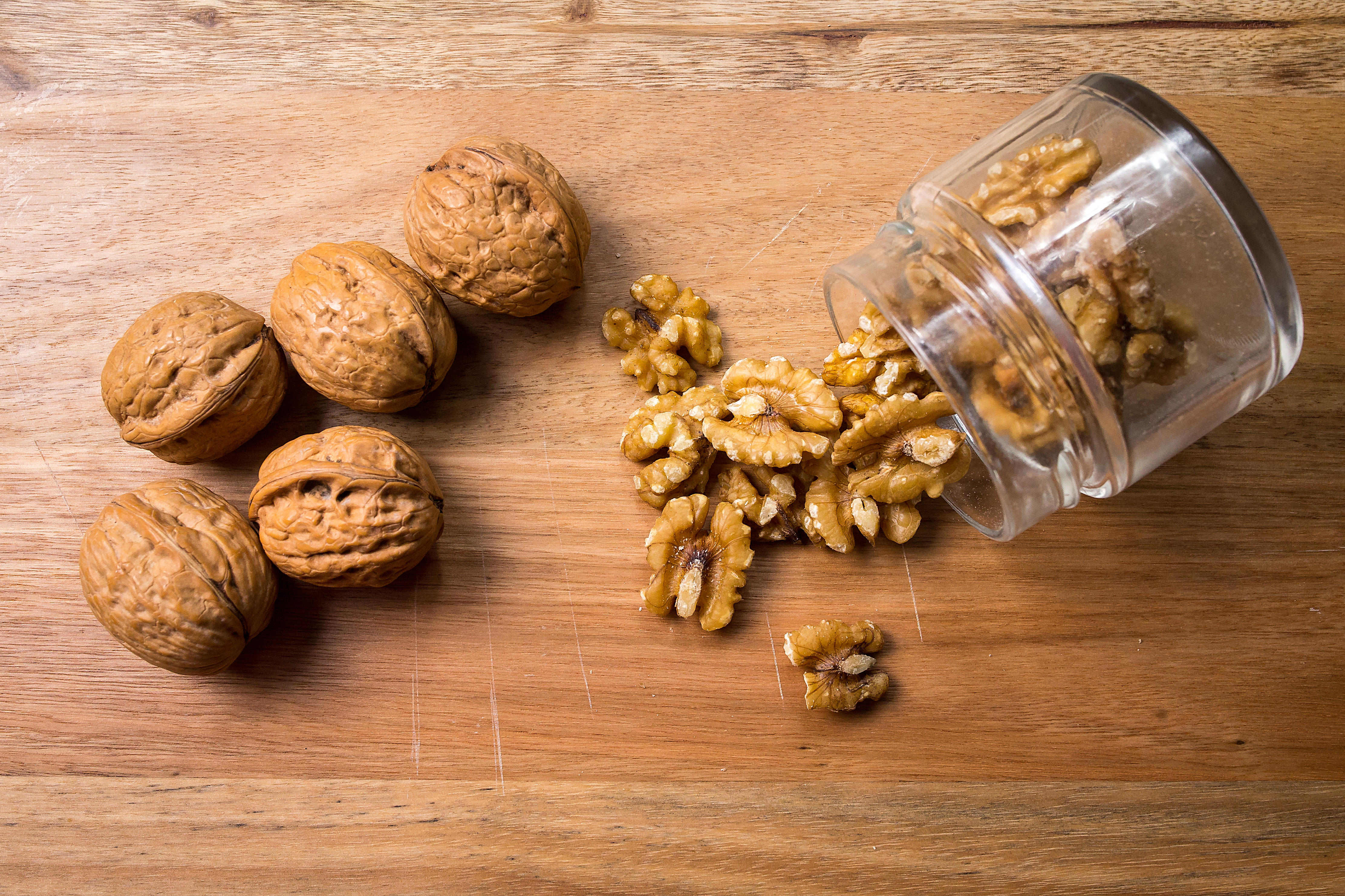 A jar of walnuts spilling out onto a wooden table